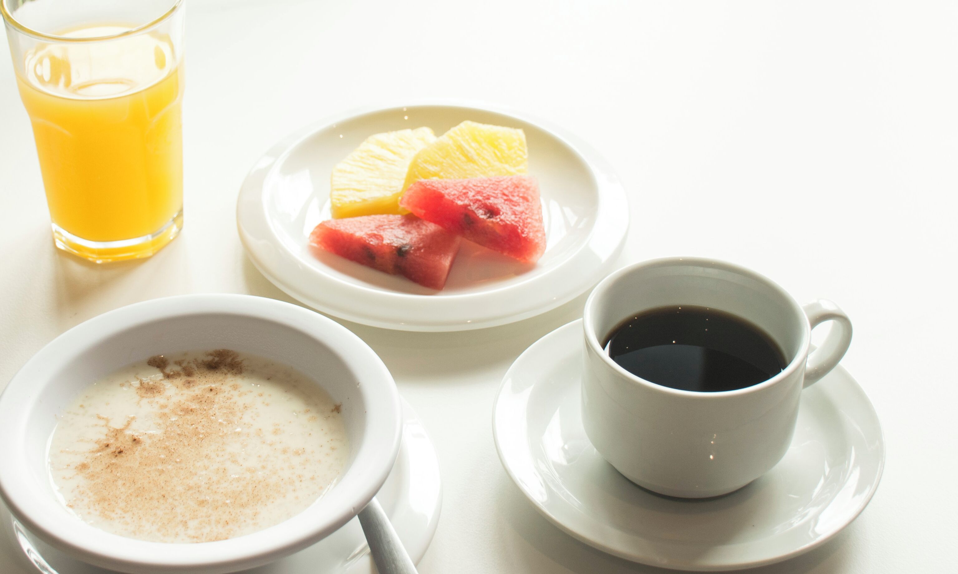 A breakfast setting with a glass of orange juice, a plate with watermelon and pineapple slices, a bowl of oatmeal, and a cup of coffee.