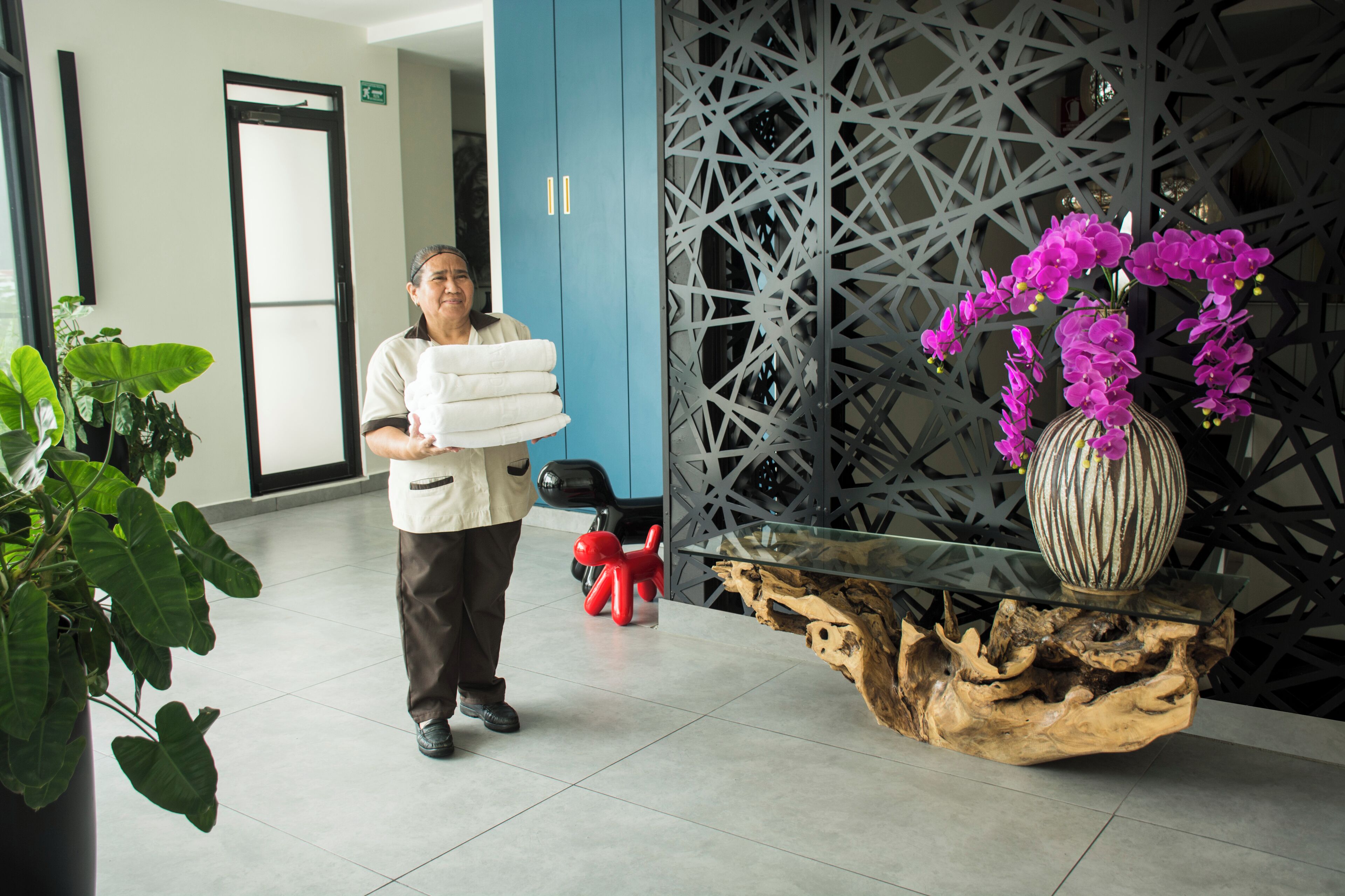 A hotel lobby with a reception desk, a decorative vase with purple flowers, and a large potted plant.