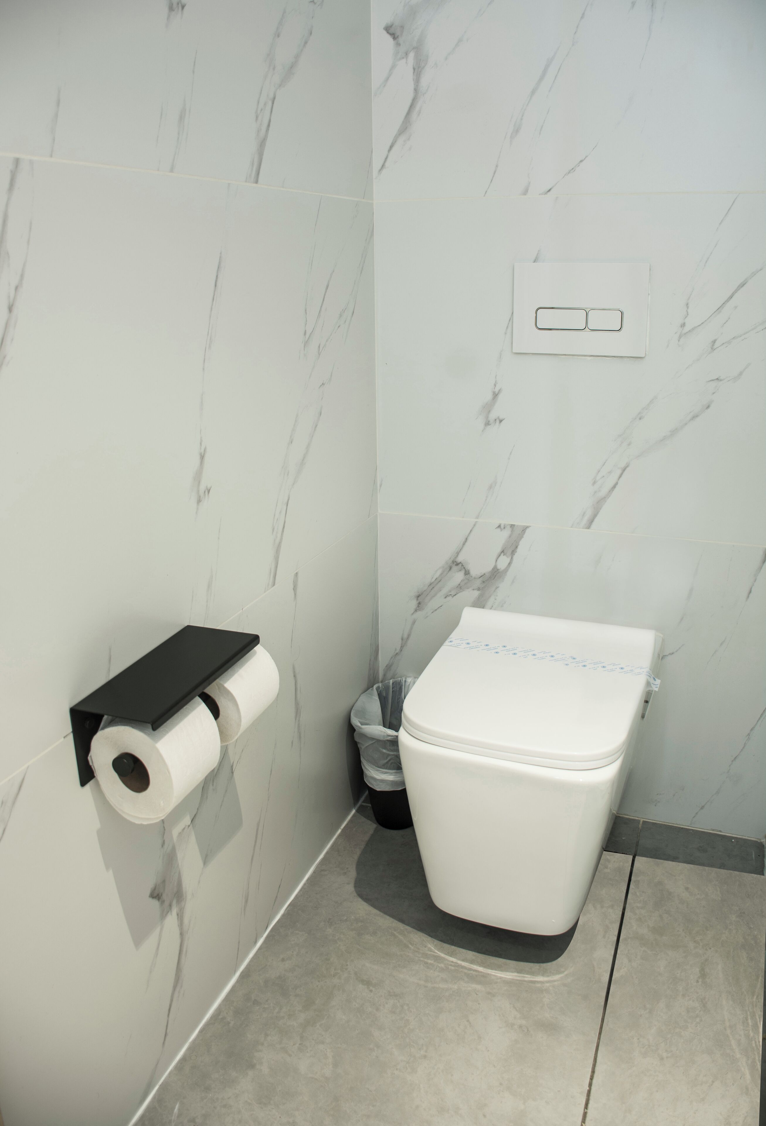 A bathroom with a toilet, marble walls, and a toilet paper holder.