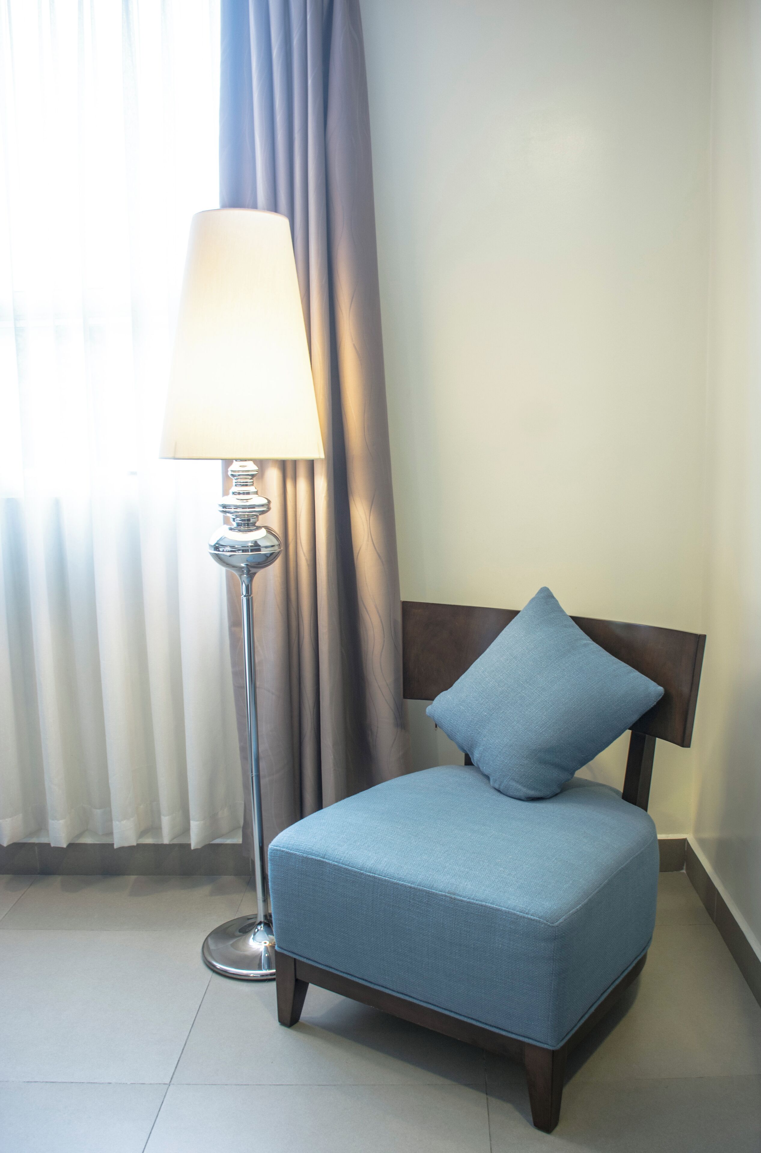 A room with a blue upholstered chair, a floor lamp, and a window with curtains.