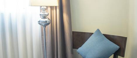 A room with a blue upholstered chair, a floor lamp, and a window with curtains.