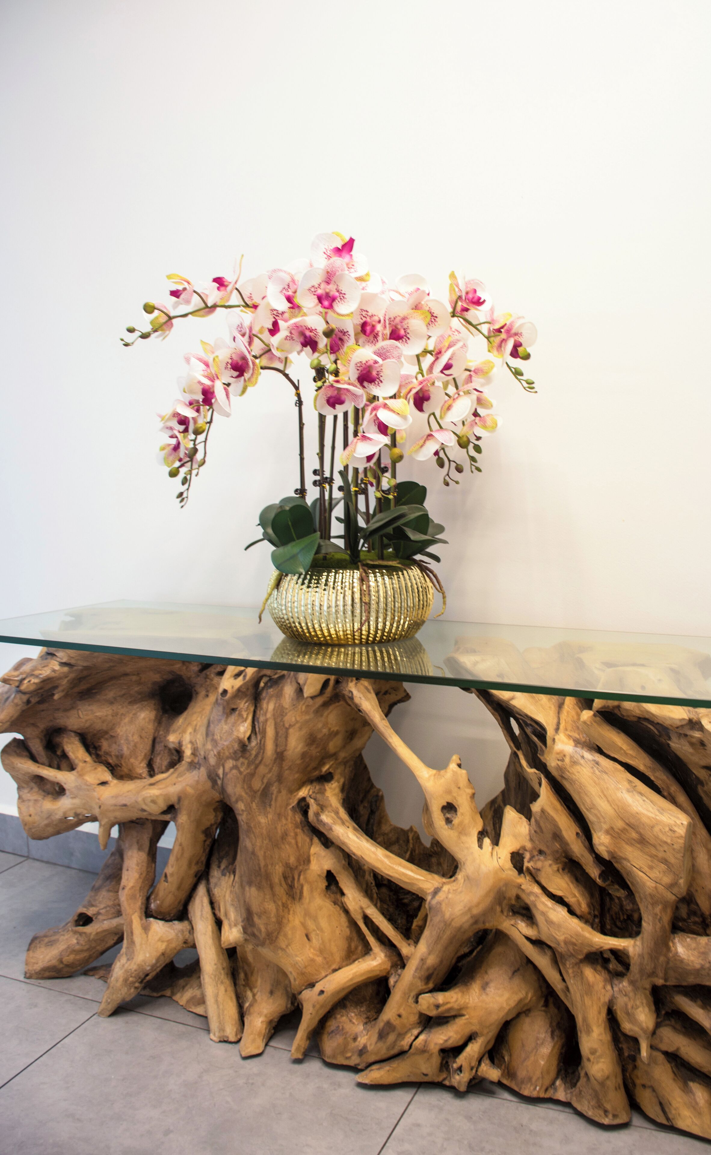 A glass-top table with a woven basket containing pink orchids, set against a white wall.
