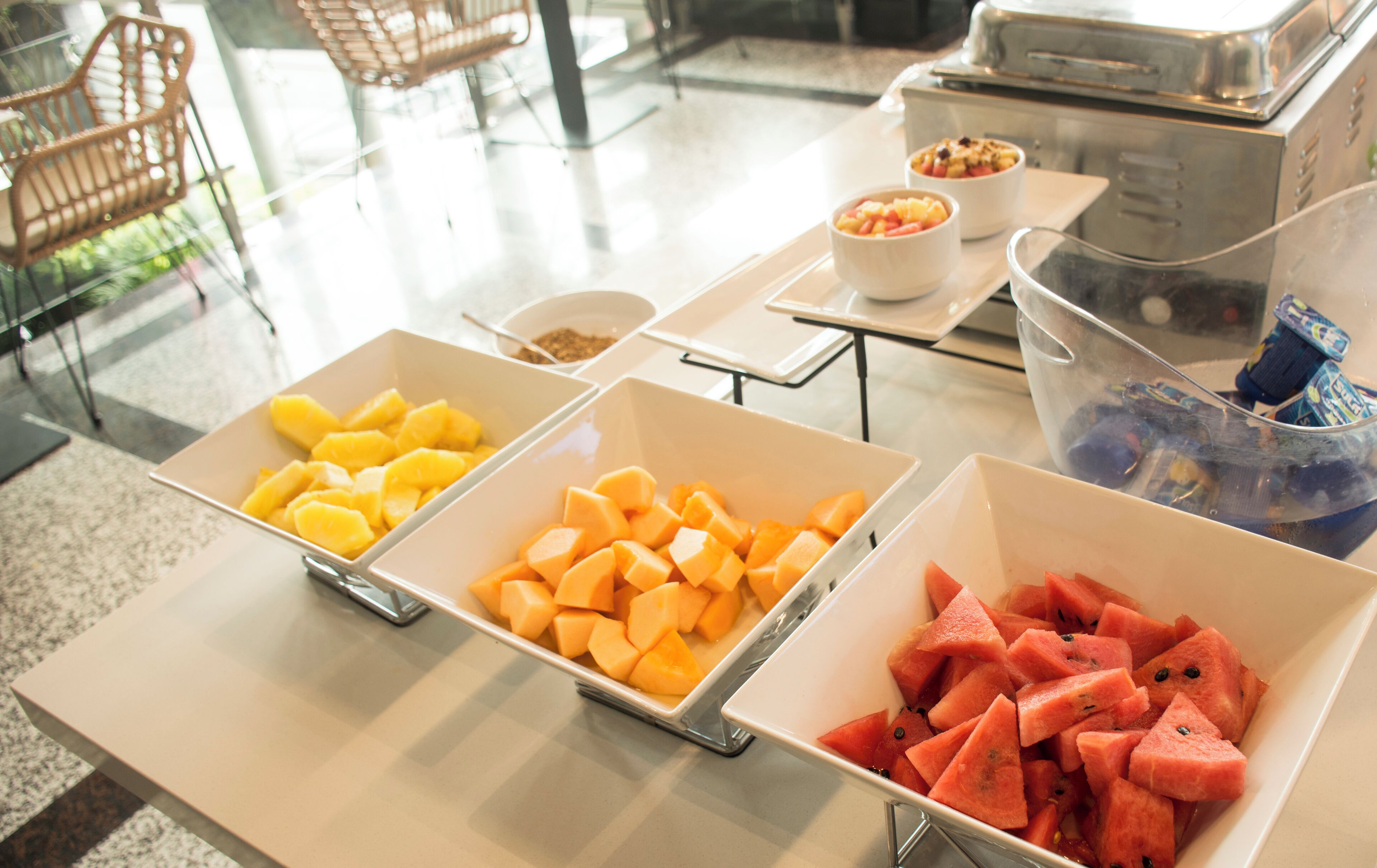 A buffet table with three trays of fruit: yellow mangoes, orange cantaloupe, and red watermelon.