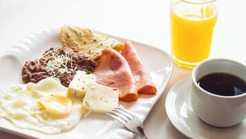 A breakfast plate with eggs, beans, ham, and cheese, accompanied by a glass of orange juice and a cup of coffee.