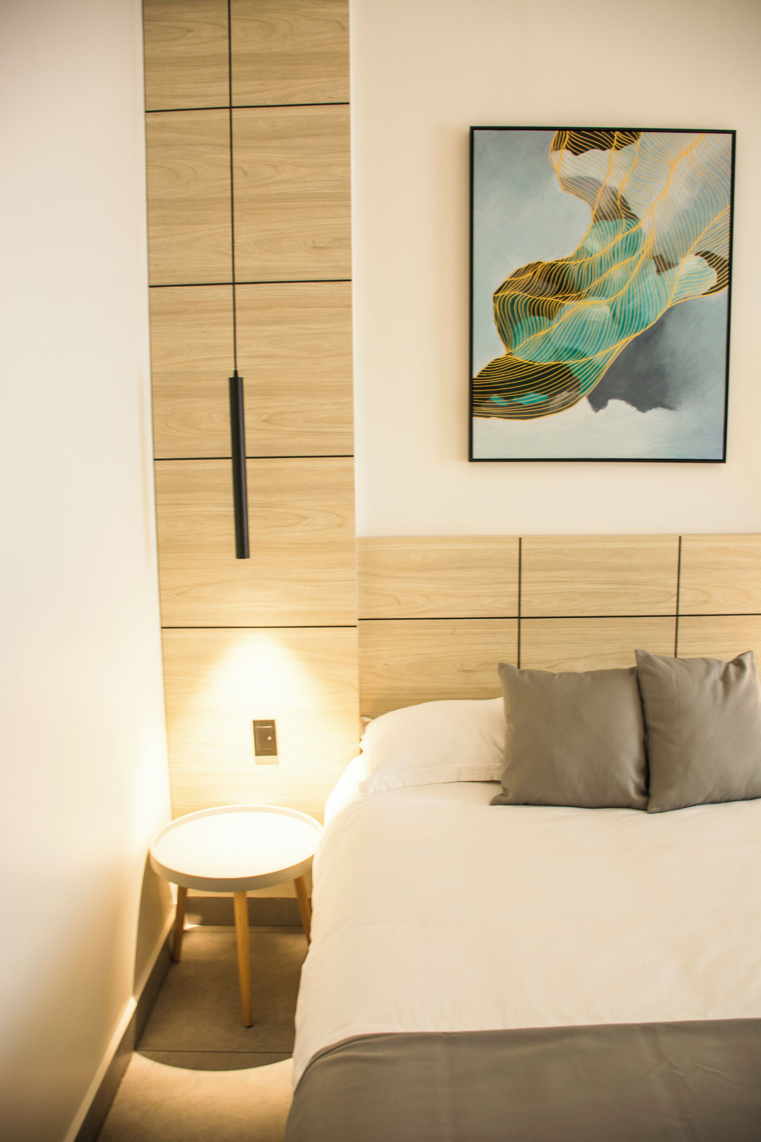 A hotel room with a bed, a round bedside table, a wall-mounted artwork, and a wooden panel wall.