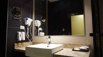 A modern bathroom with a granite countertop, a white sink, and two hair dryers mounted on the wall.