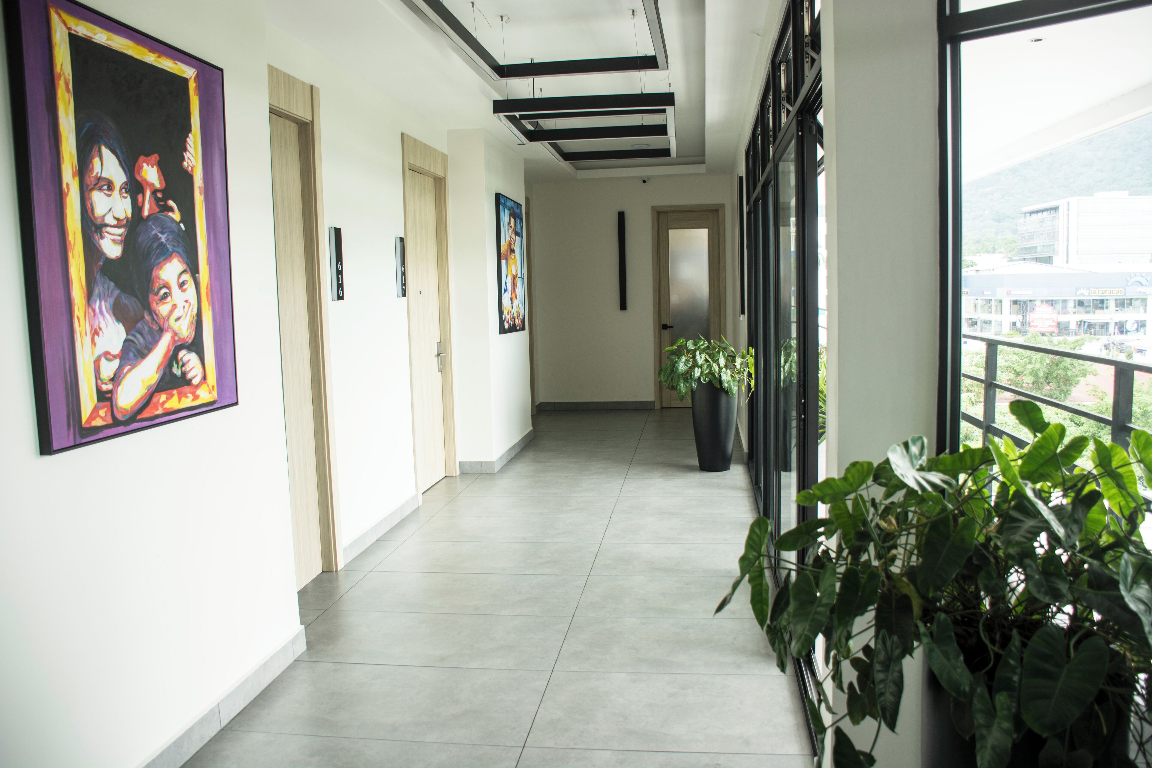 A corridor with a tiled floor, framed artwork on the walls, and potted plants.