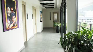 A corridor with a tiled floor, framed artwork on the walls, and potted plants.