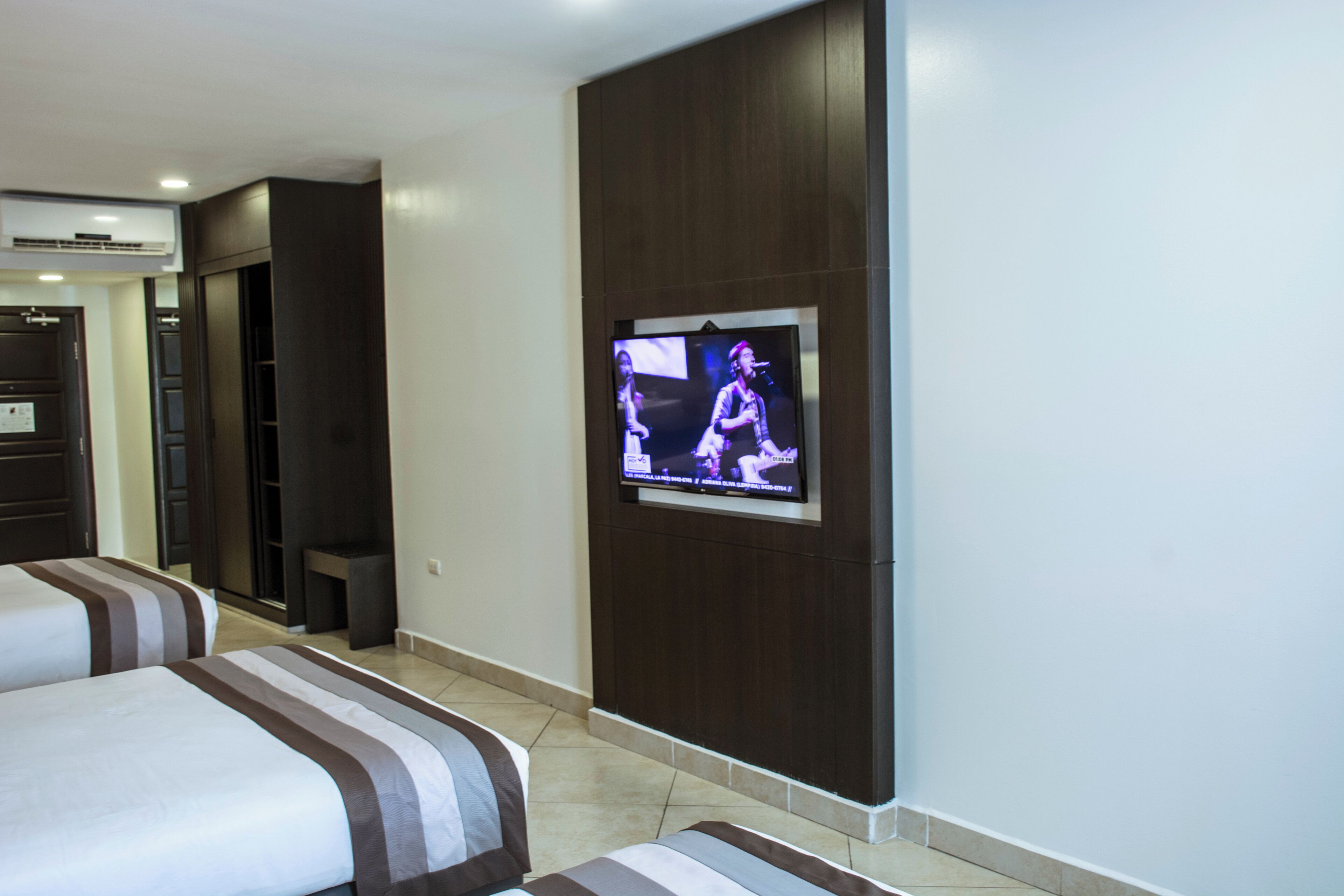 Habitación de hotel con dos camas, un televisor montado en la pared y paneles de madera oscura.