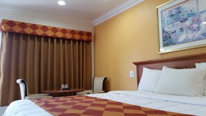 A hotel room with a large bed, a small table with two cups, a chair, and a painting on the wall. - Kona Inn Motel Anaheim (Anaheim)