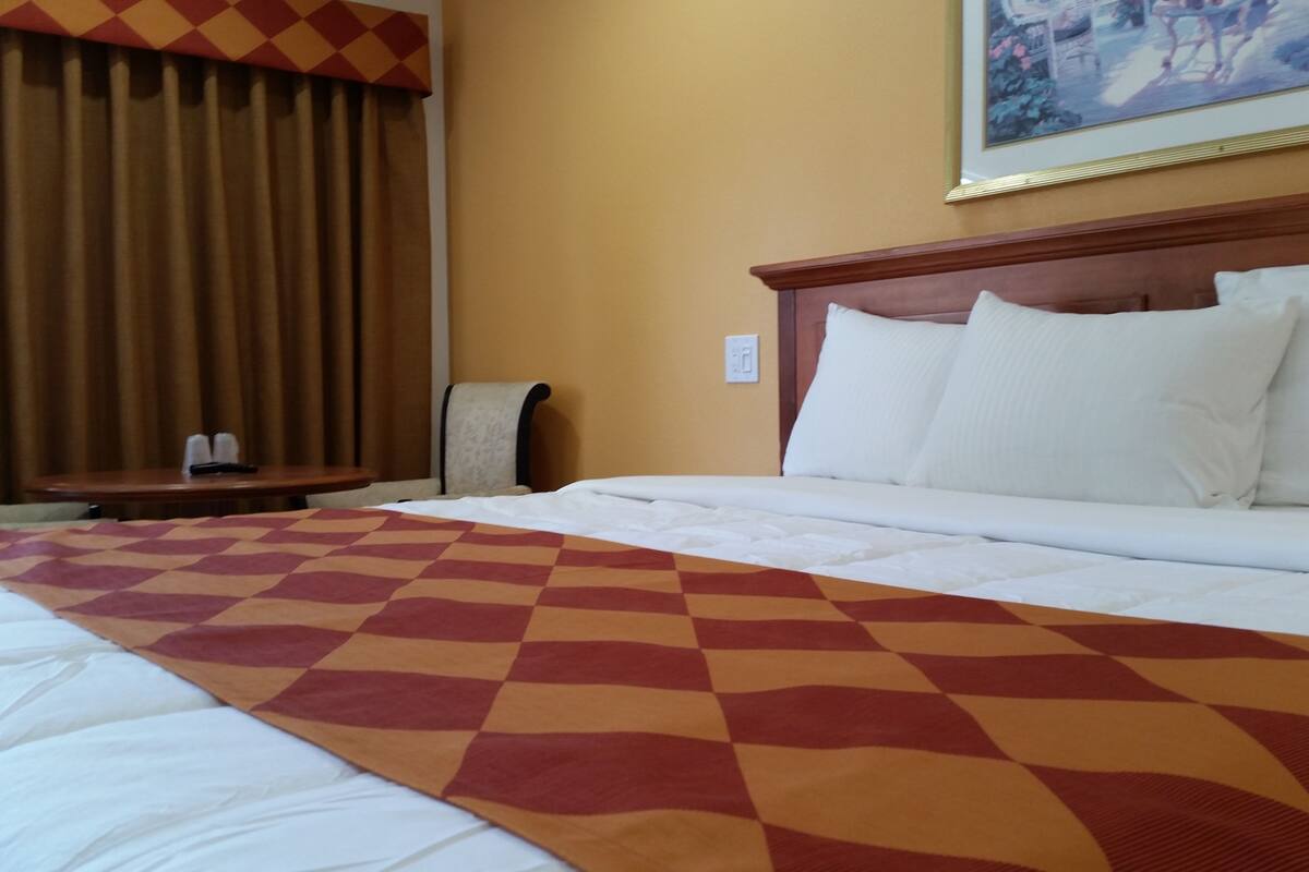 Une chambre d’hôtel avec un grand lit, une tête de lit en bois, une table avec une chaise et un tableau au mur.