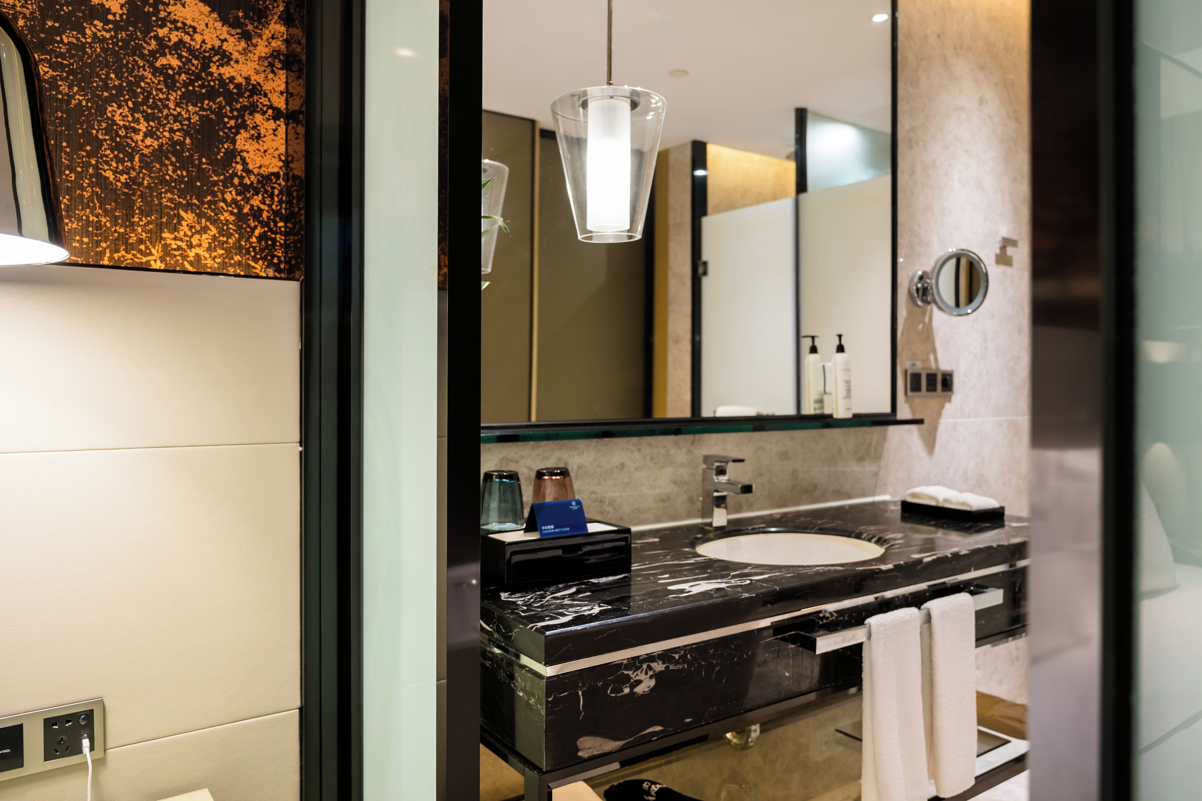 A modern bathroom with a black marble sink, a glass shower enclosure, and a large mirror.
