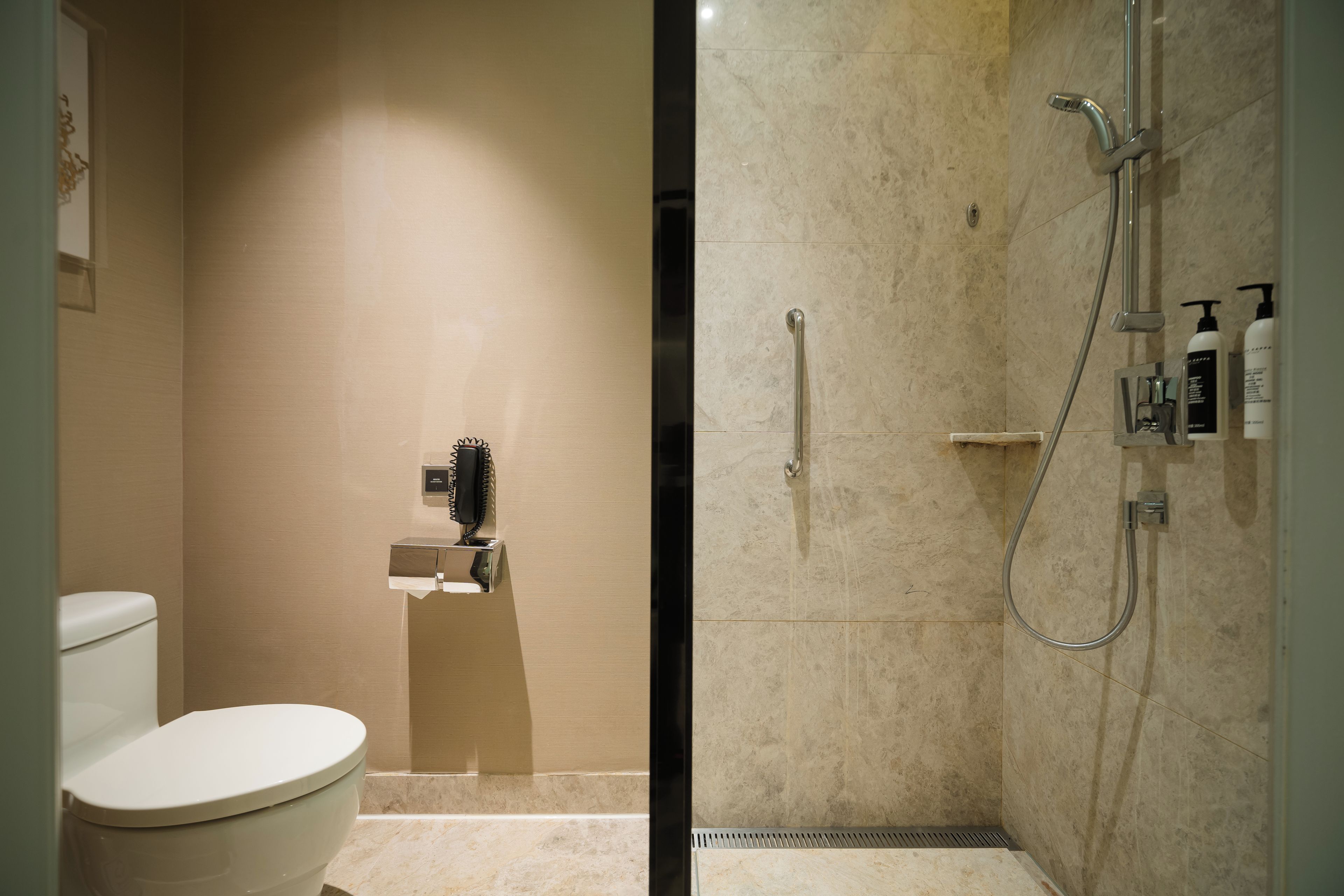 Een badkamer met een toilet, een douche met een handdouche en een wandtelefoon.