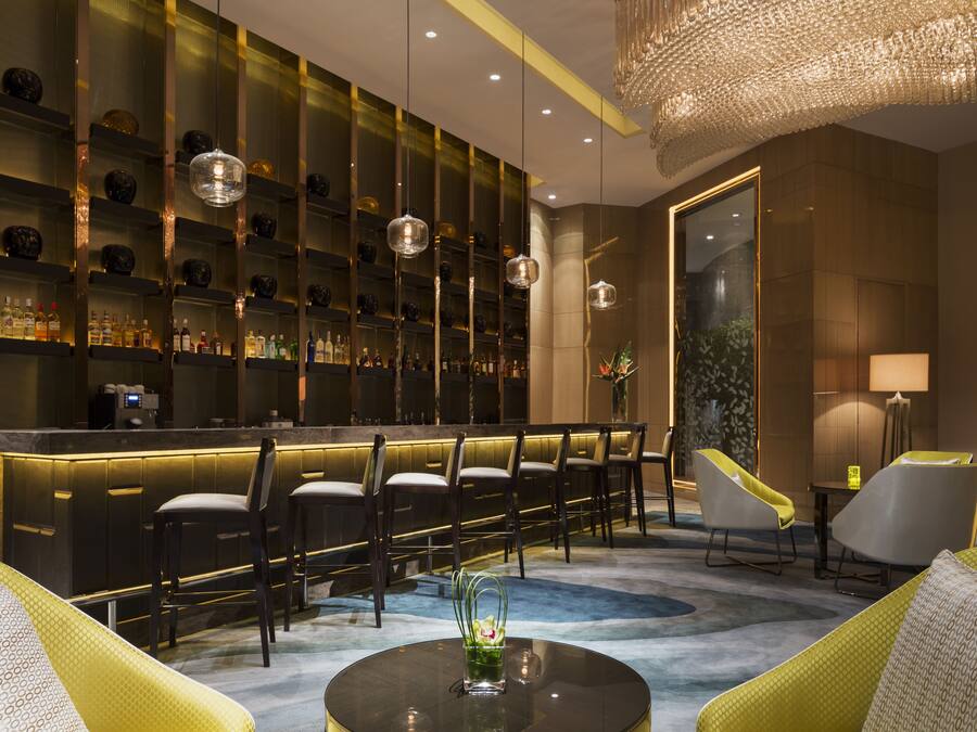 Een bar met flessen op planken, een toog en zitplaatsen met stoelen en een bank.