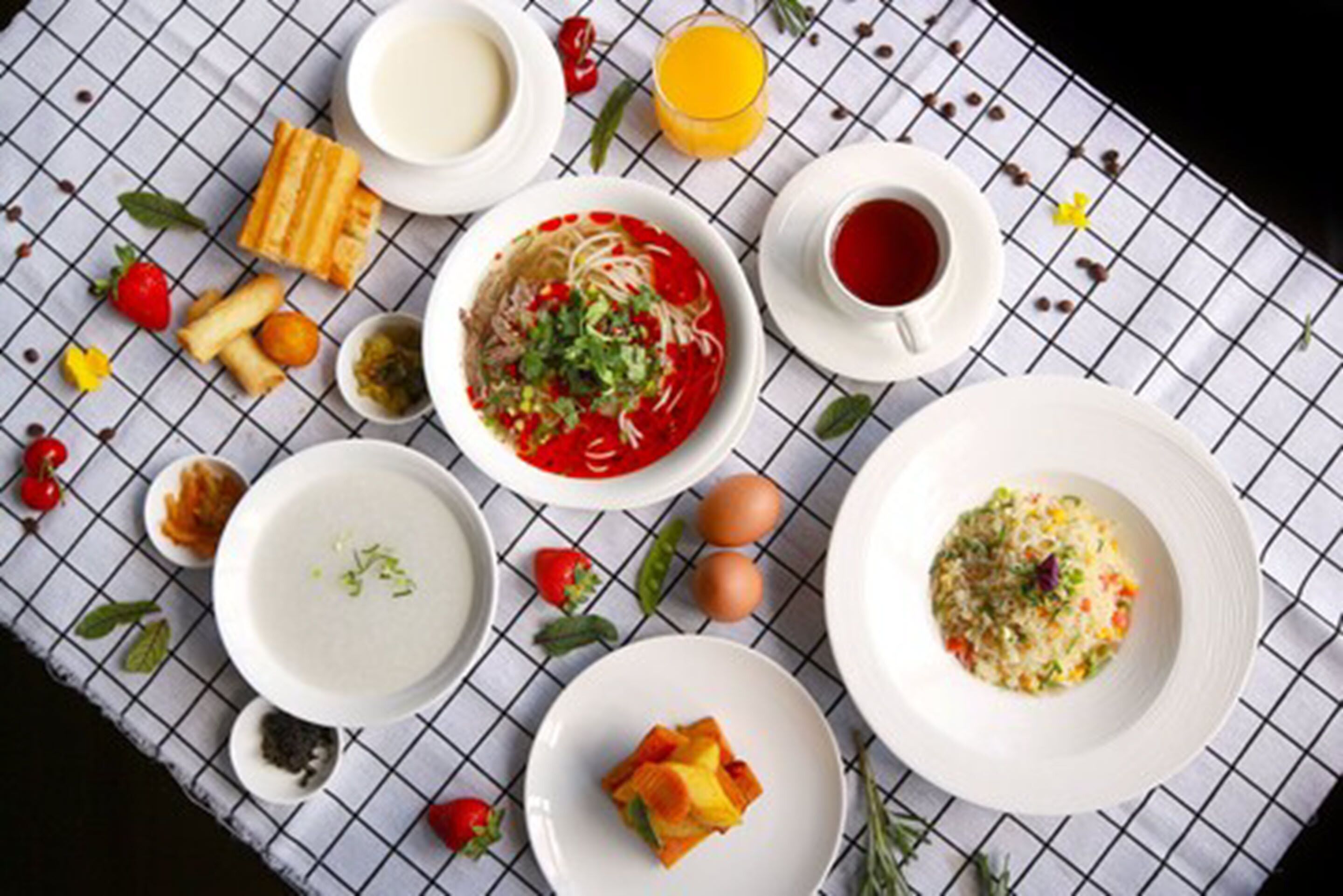 Una mesa con varios platos, incluyendo un tazón de sopa, una porción de arroz y un tazón de fideos con salsa roja.