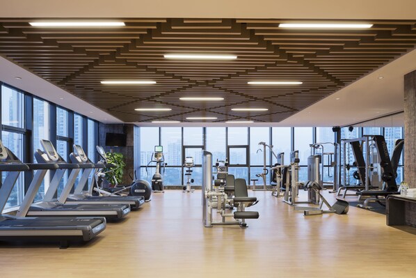 A gym with treadmills, weight machines, and a large window offering a city view. - Wanda Realm Jiangmen (Jiangmen)