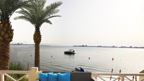 A terrace with a view of the sea, featuring a sofa with blue cushions, a table with a teapot and cups, and a palm tree. - Dana Beach Resort (Abqaiq)