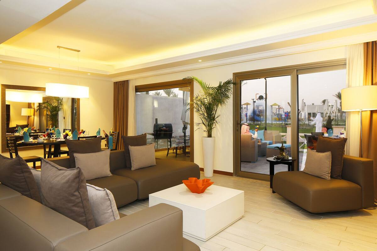 A spacious living room with a large sofa set, a coffee table, and a dining area with a table and chairs.