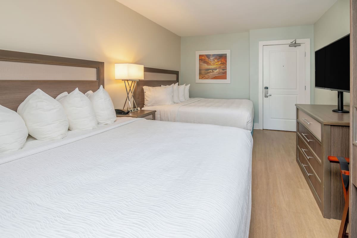Habitación de hotel con dos camas, un escritorio, una silla, un televisor y una puerta.