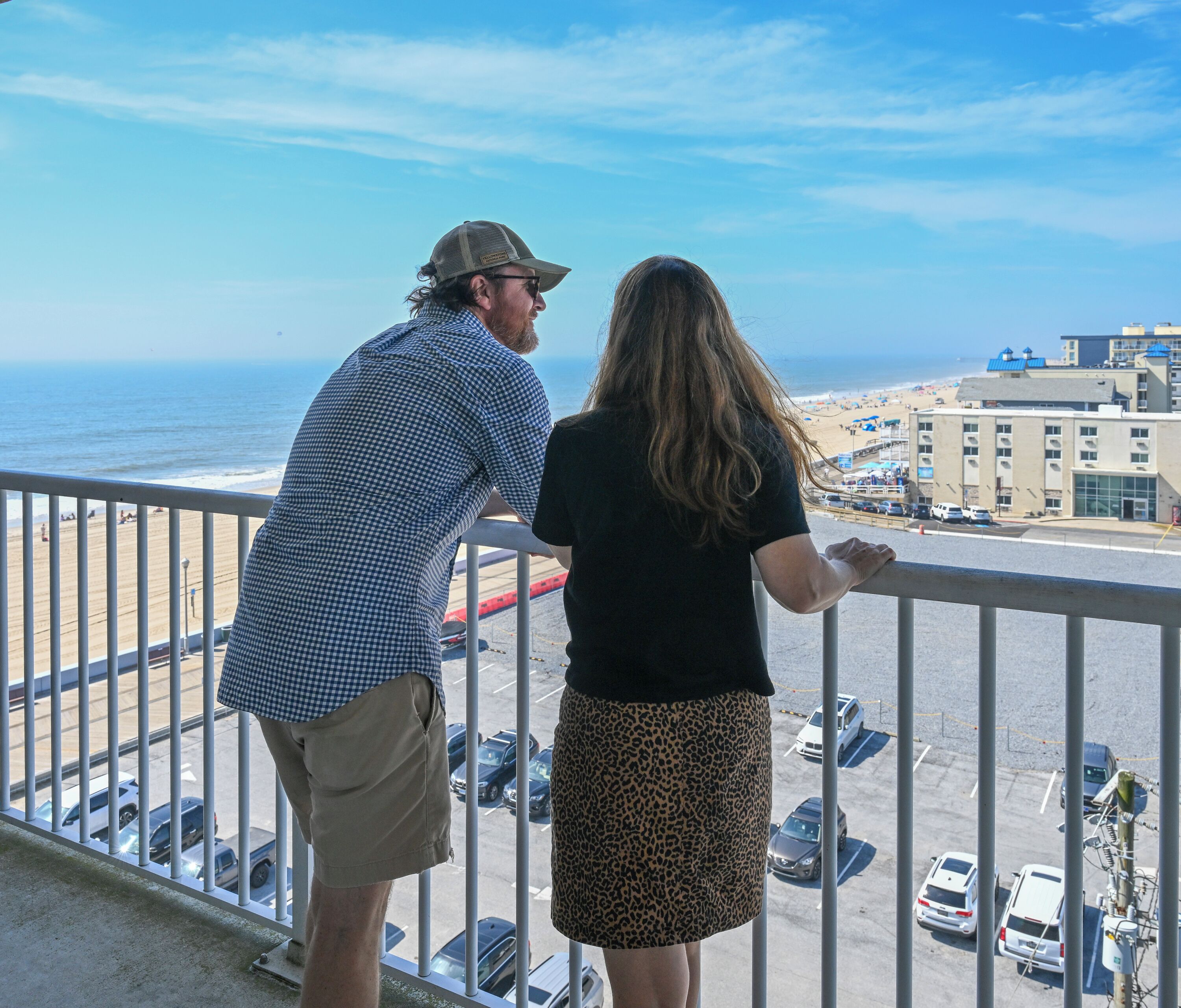 A balcony with a view of the beach and parking lot.