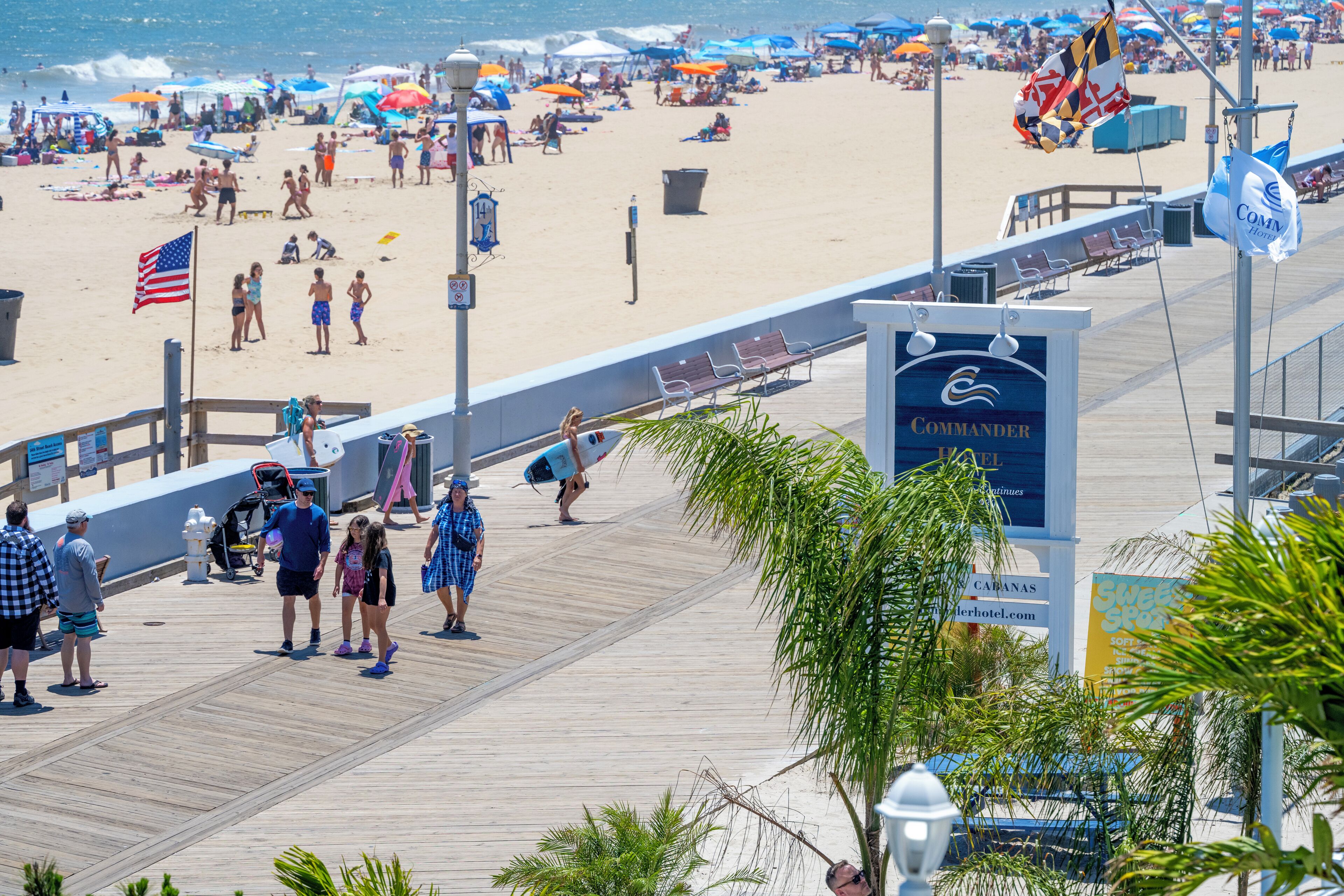 Un paseo marítimo con un letrero de hotel, sombrillas de playa y gente caminando.