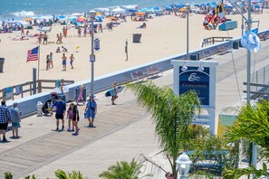 A boardwalk with a hotel sign, beach umbrellas, and people walking. - Commander Hotel & Suites (Ocean City)