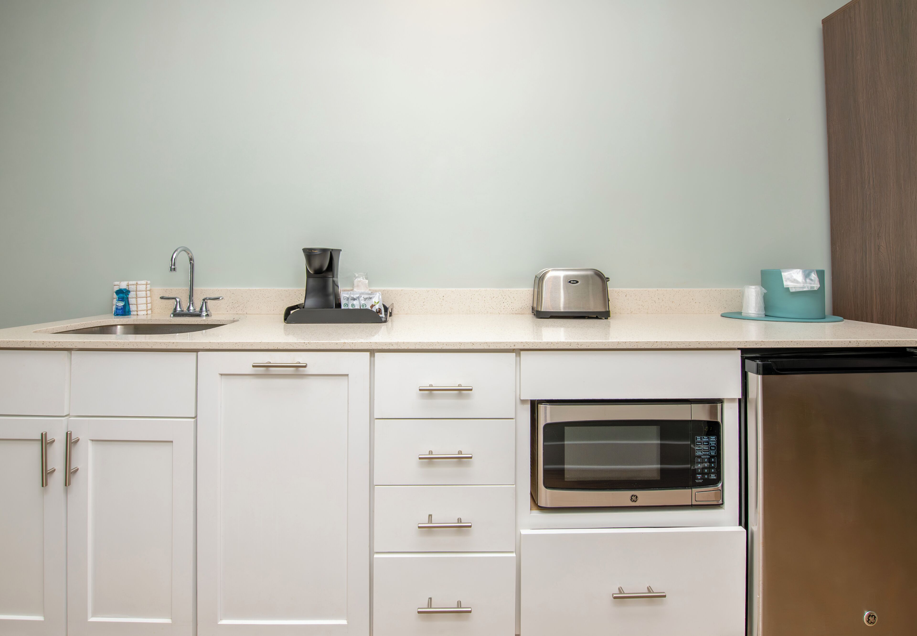 A kitchen with a sink, coffee maker, toaster, microwave, and dishwasher.