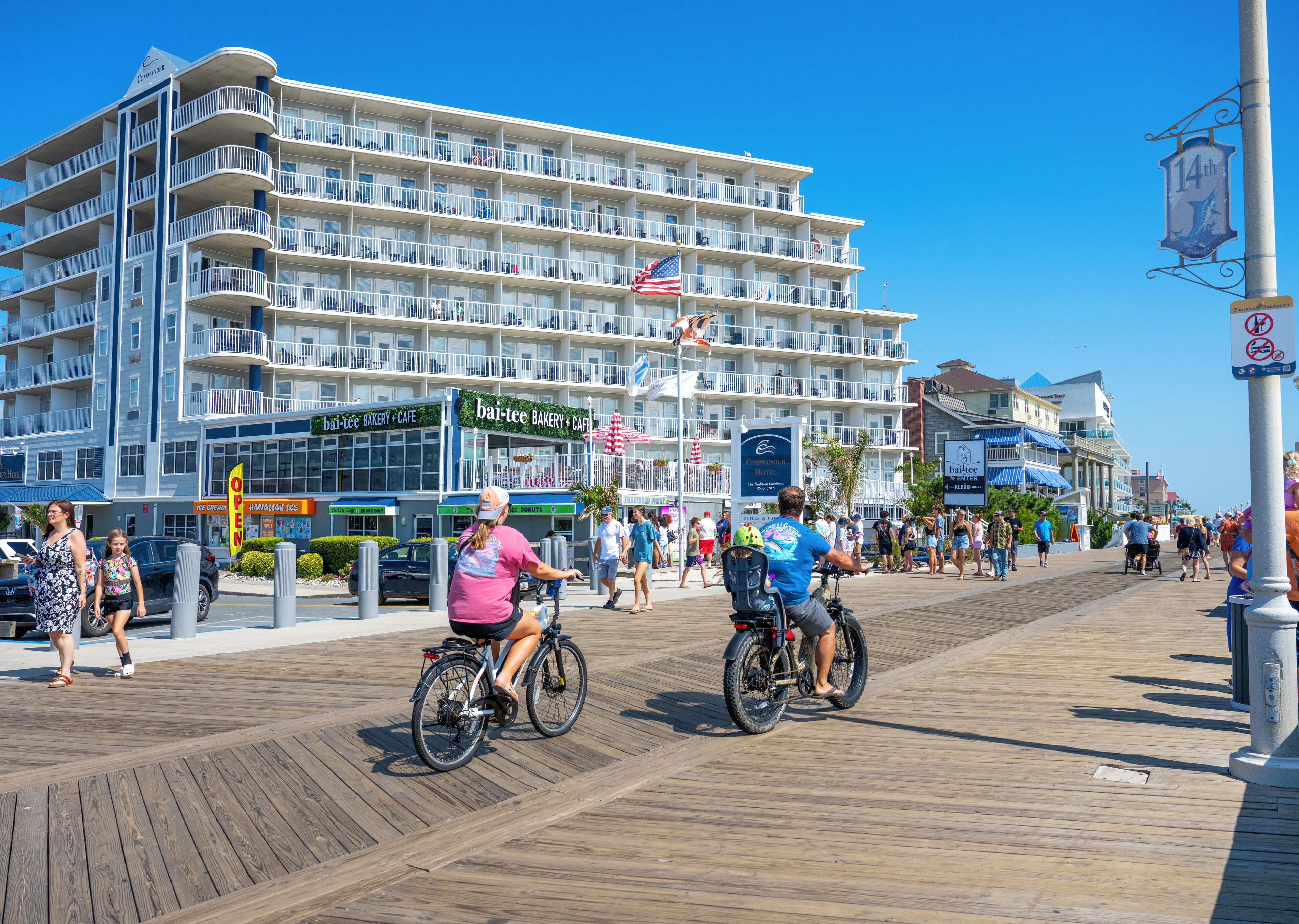 A multi-story hotel with balconies, a boardwalk, and a beachside view.
