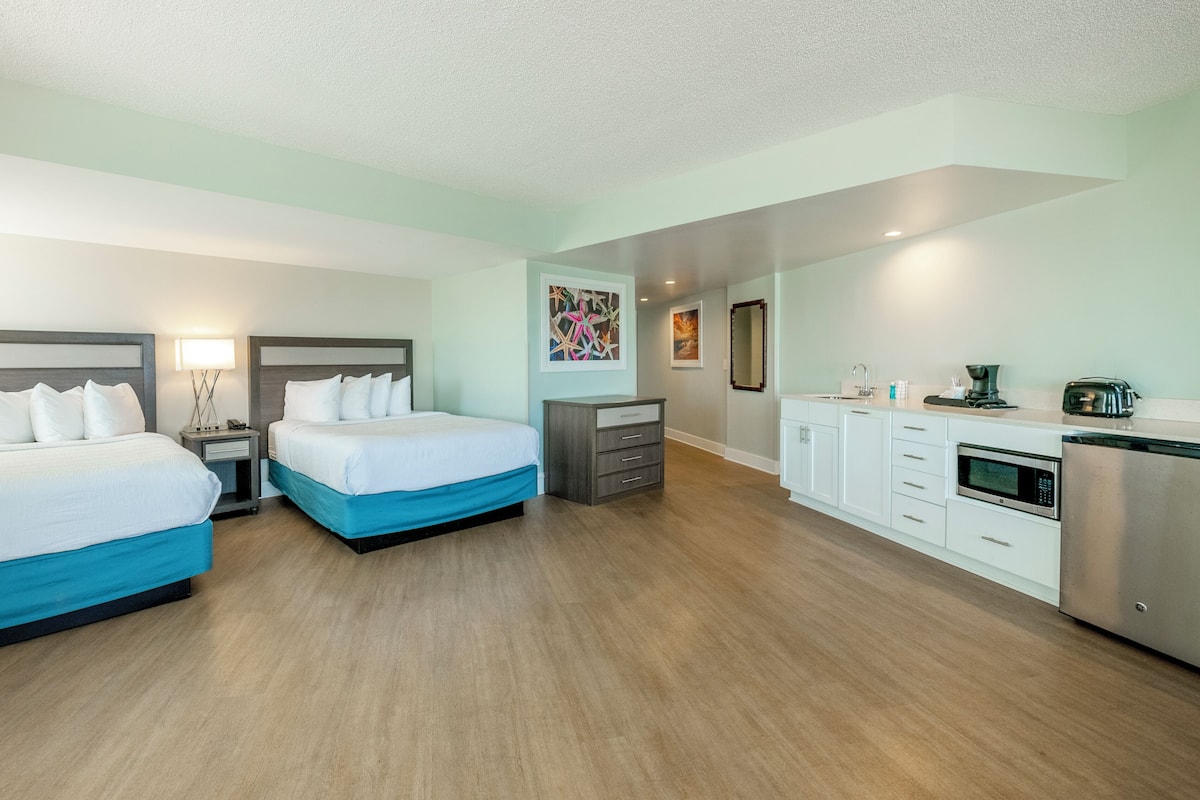 Habitación de hotel con dos camas, kitchenette y baño.
