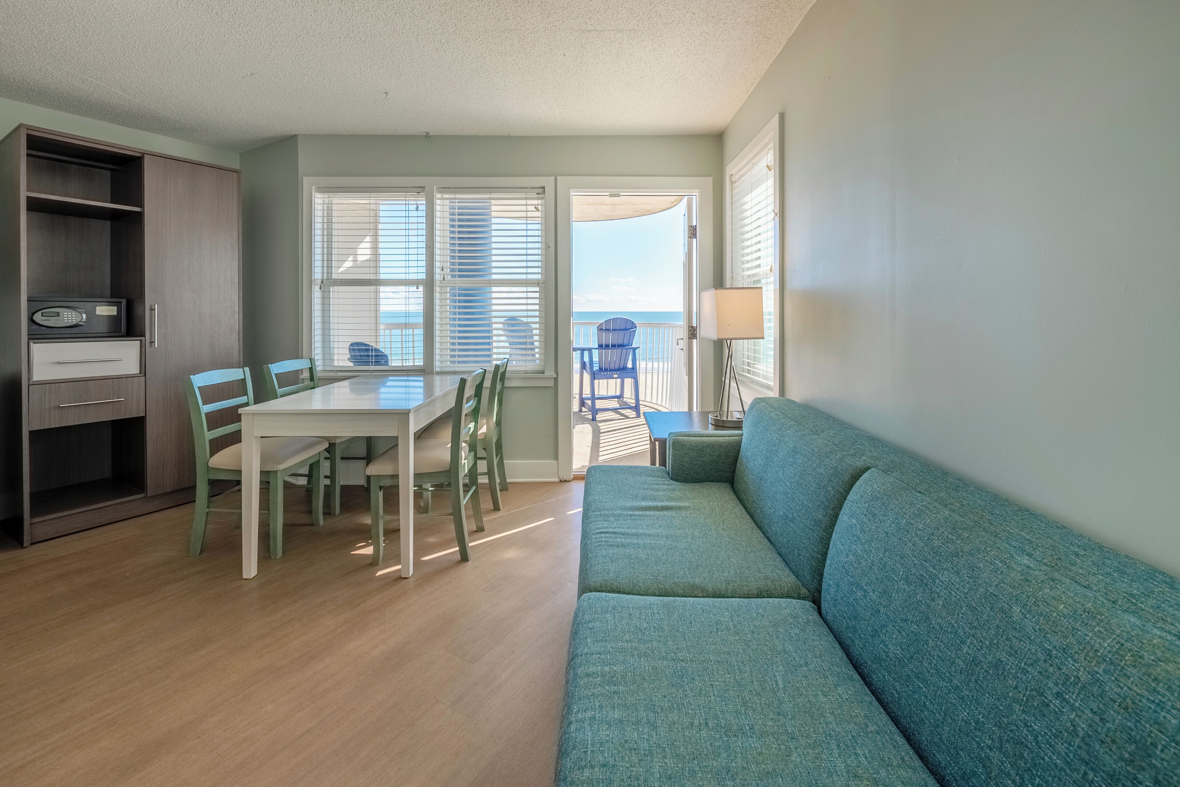 A living room with a sofa, a dining table with chairs, a cabinet, and a view of the ocean through the windows.