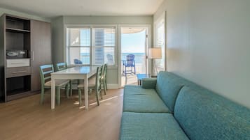 A living room with a sofa, a dining table with chairs, a cabinet, and a view of the ocean through the windows.