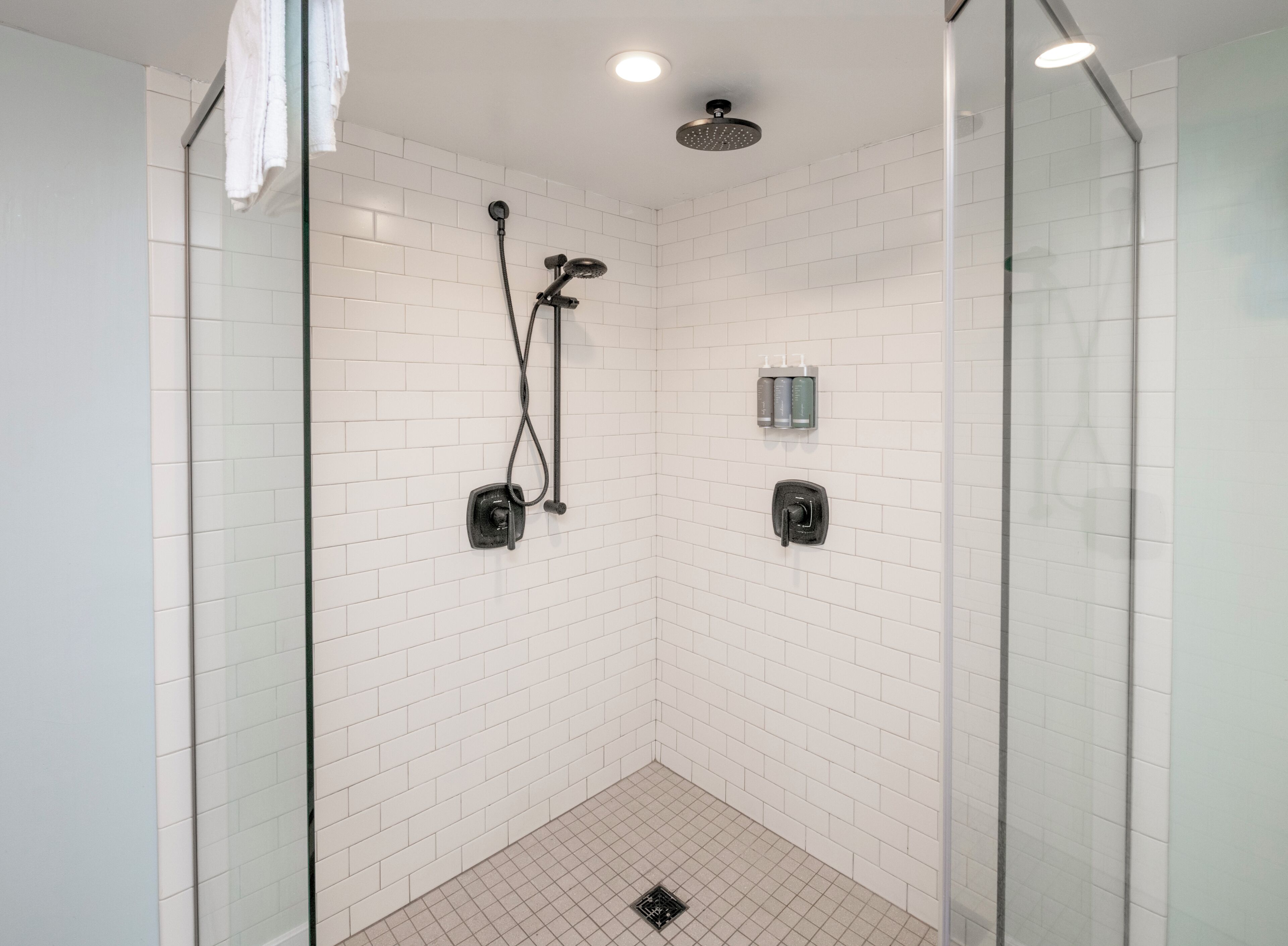 Une douche moderne avec des murs recouverts de carreaux blancs, une porte en verre et une pomme de douche fixée au plafond.
