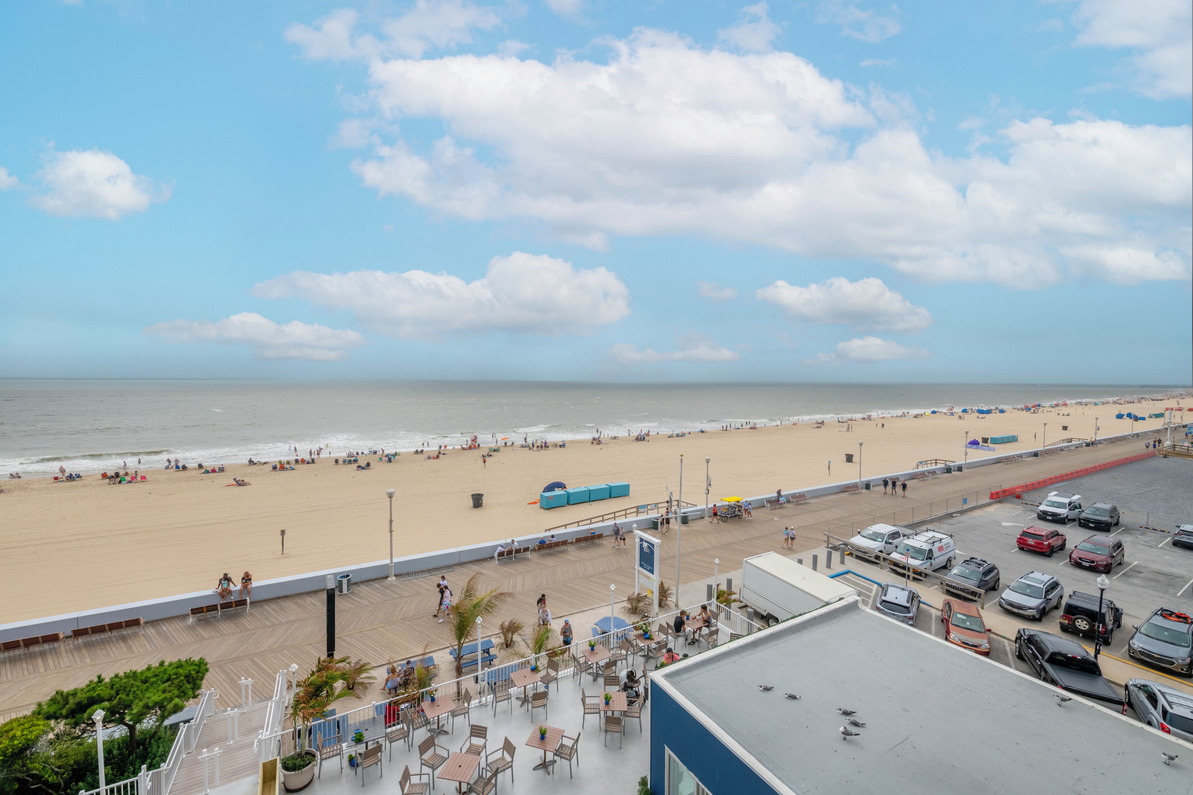 Vista de la playa desde un balcón de hotel, con un aparcamiento y zona de estar al aire libre.
