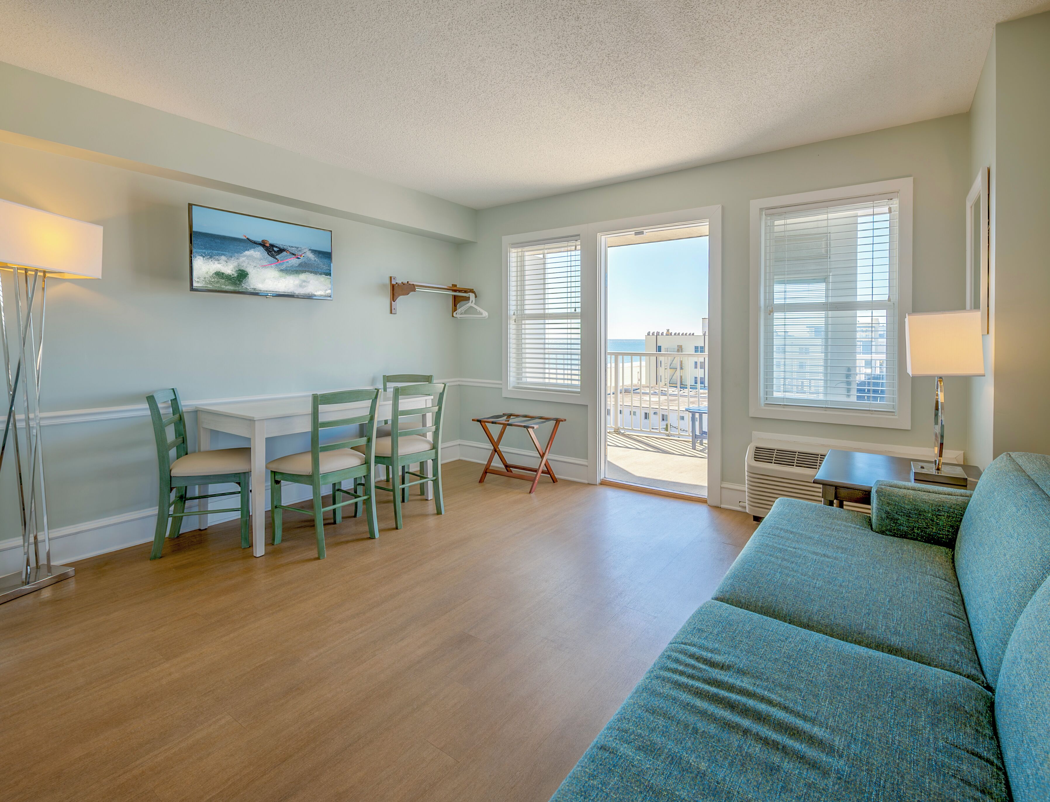 A living room with a sofa, a dining table with chairs, a small table, and a balcony with a view.
