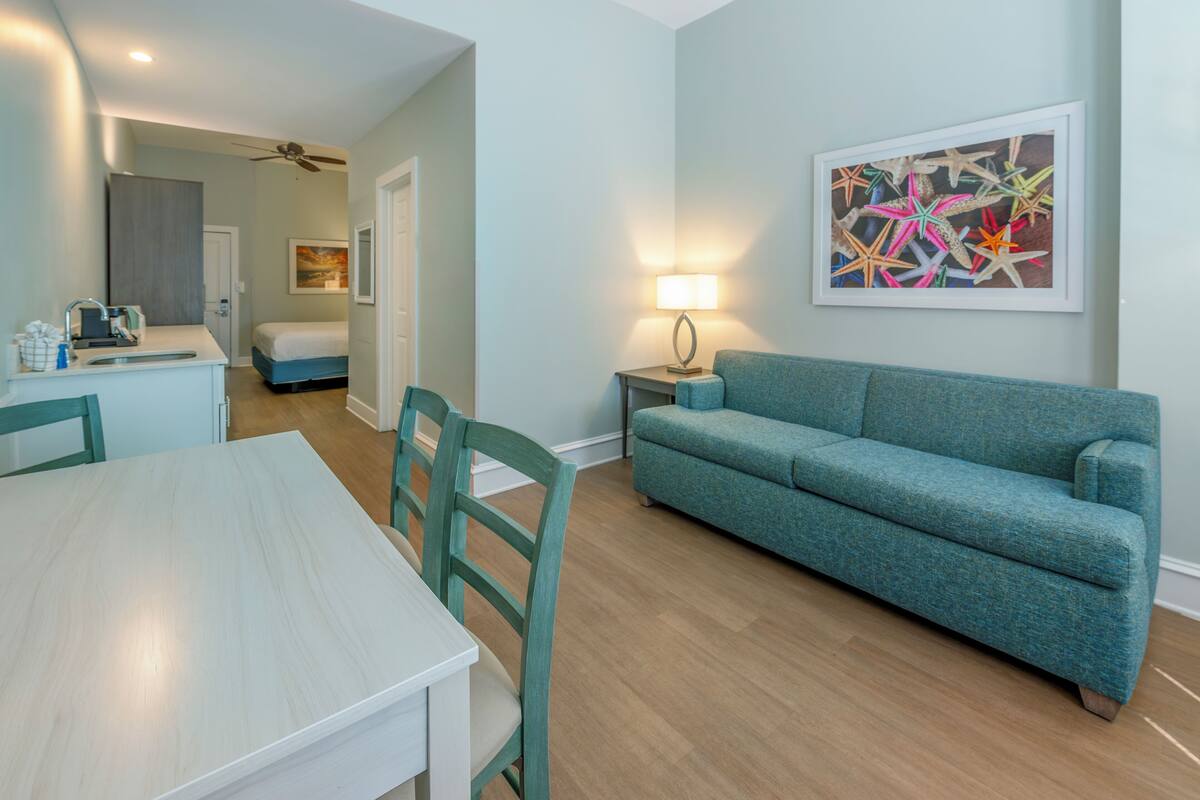 Una habitación con una mesa de comedor, sofá color turquesa y un ventilador de techo.