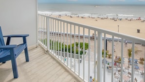 Un balcon donnant sur une plage, avec une balustrade blanche, des chaises bleues et une table.