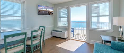 A room with a view of the ocean, a dining area with chairs, a sofa, and a table with a lamp.
