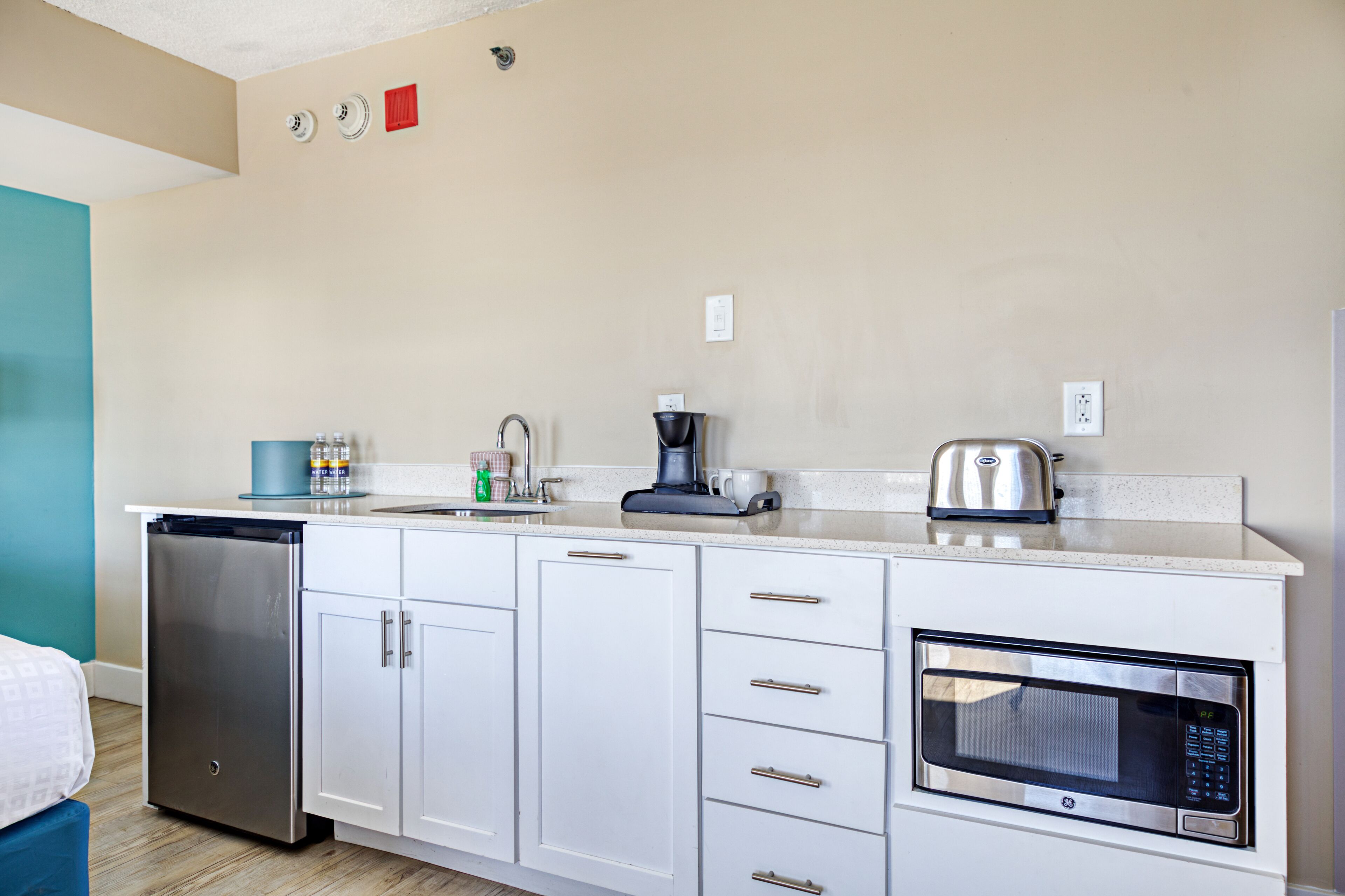 Una kitchenette compacta equipada con lavavajillas, microondas, cafetera y un lavamanos pequeño.