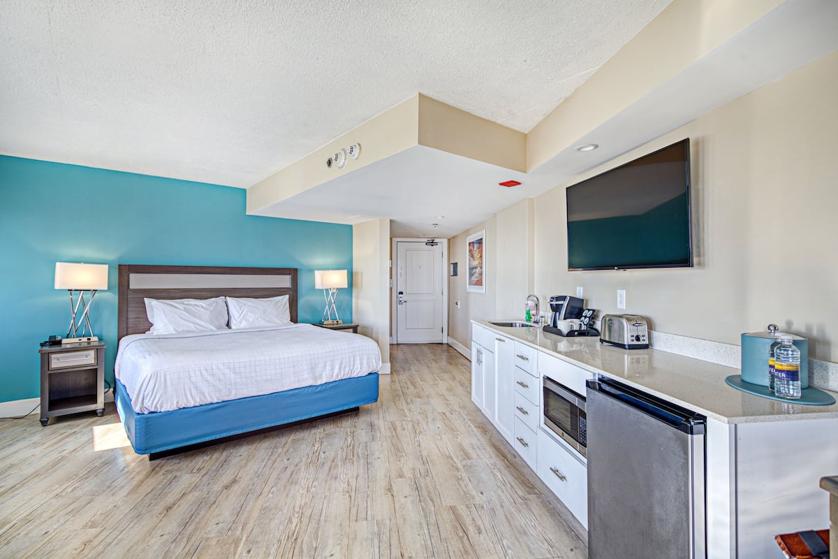 Habitación de hotel con cama, mesitas de noche, escritorio con lavamanos, refrigerador y televisor montado en la pared.