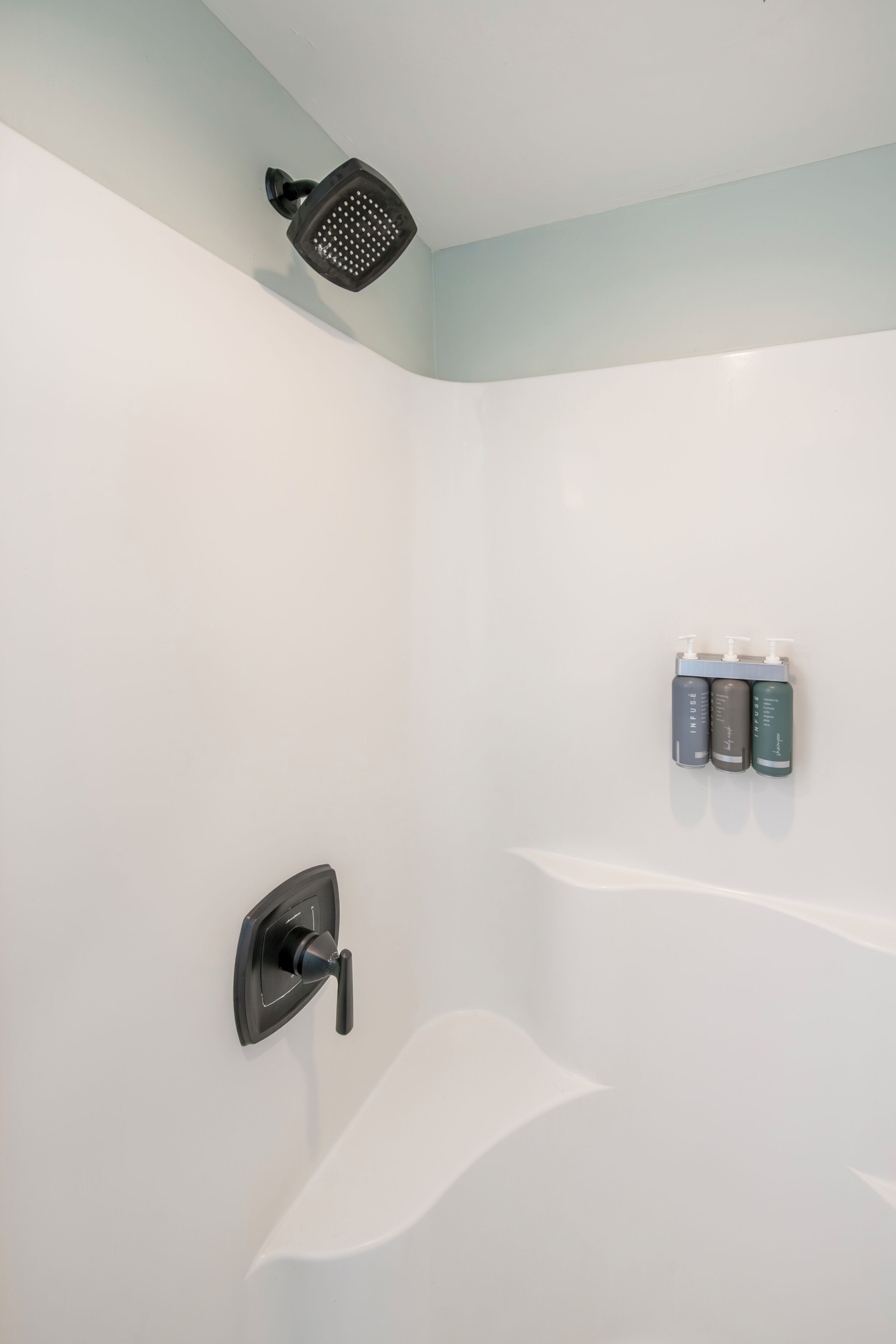 A shower with a handheld showerhead, a wall-mounted faucet, and a shelf with three bottles.