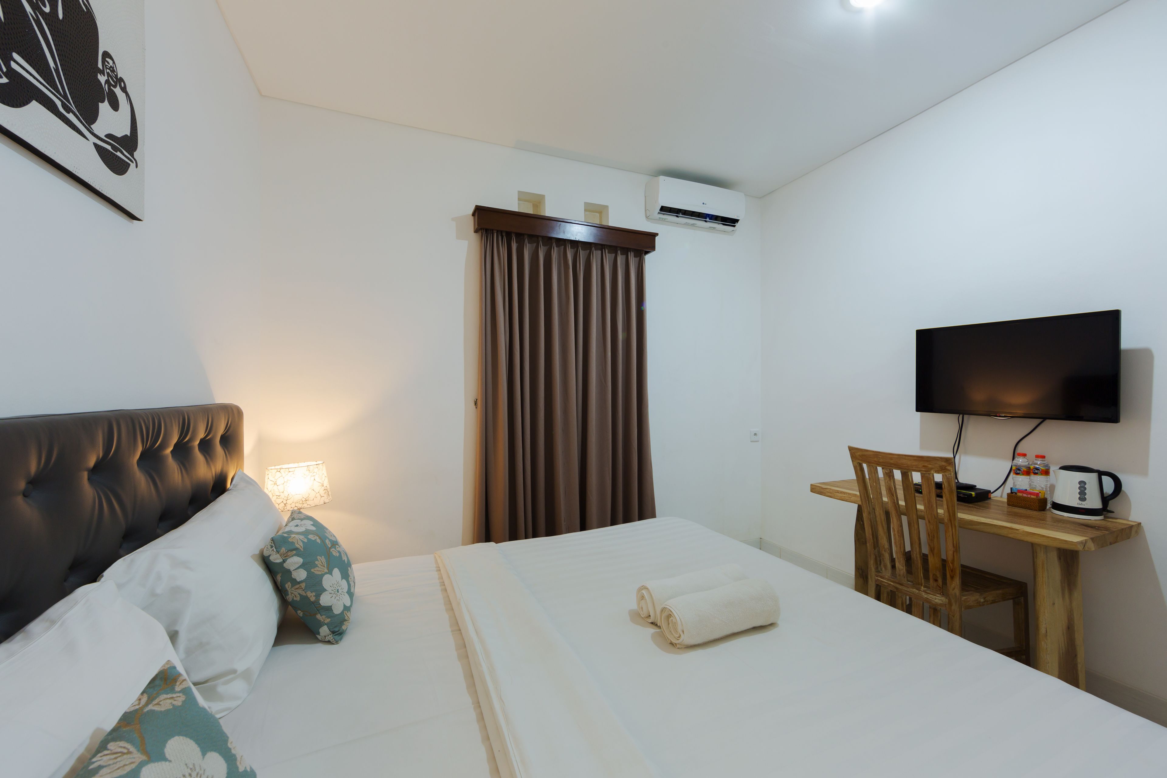 Una habitació d'hotel amb un llit, una taula de treball amb una cadira, una televisió i un aparell d'aire condicionat.