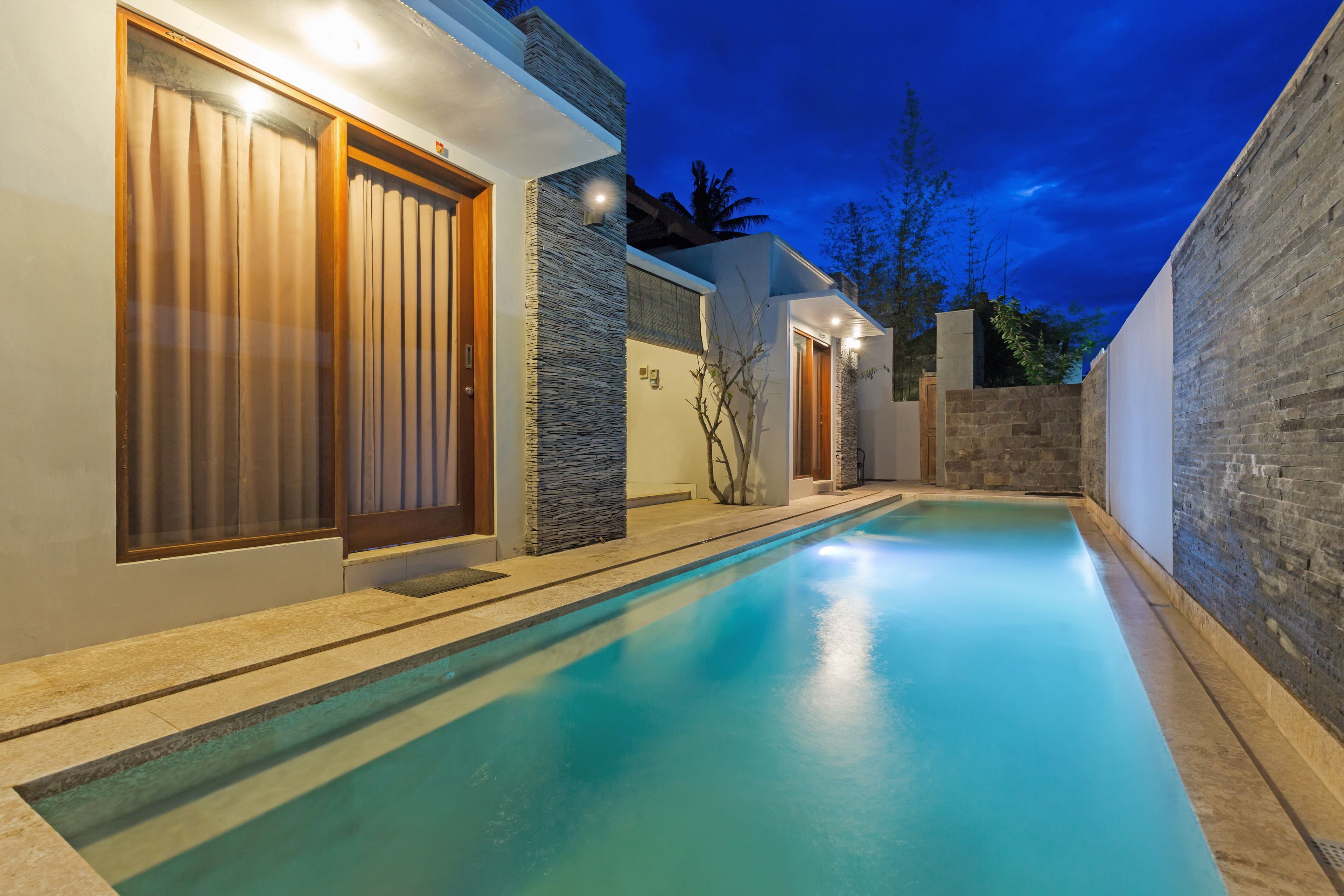 A modern pool area with a stone wall and wooden doors, surrounded by a brick wall and a clear sky.