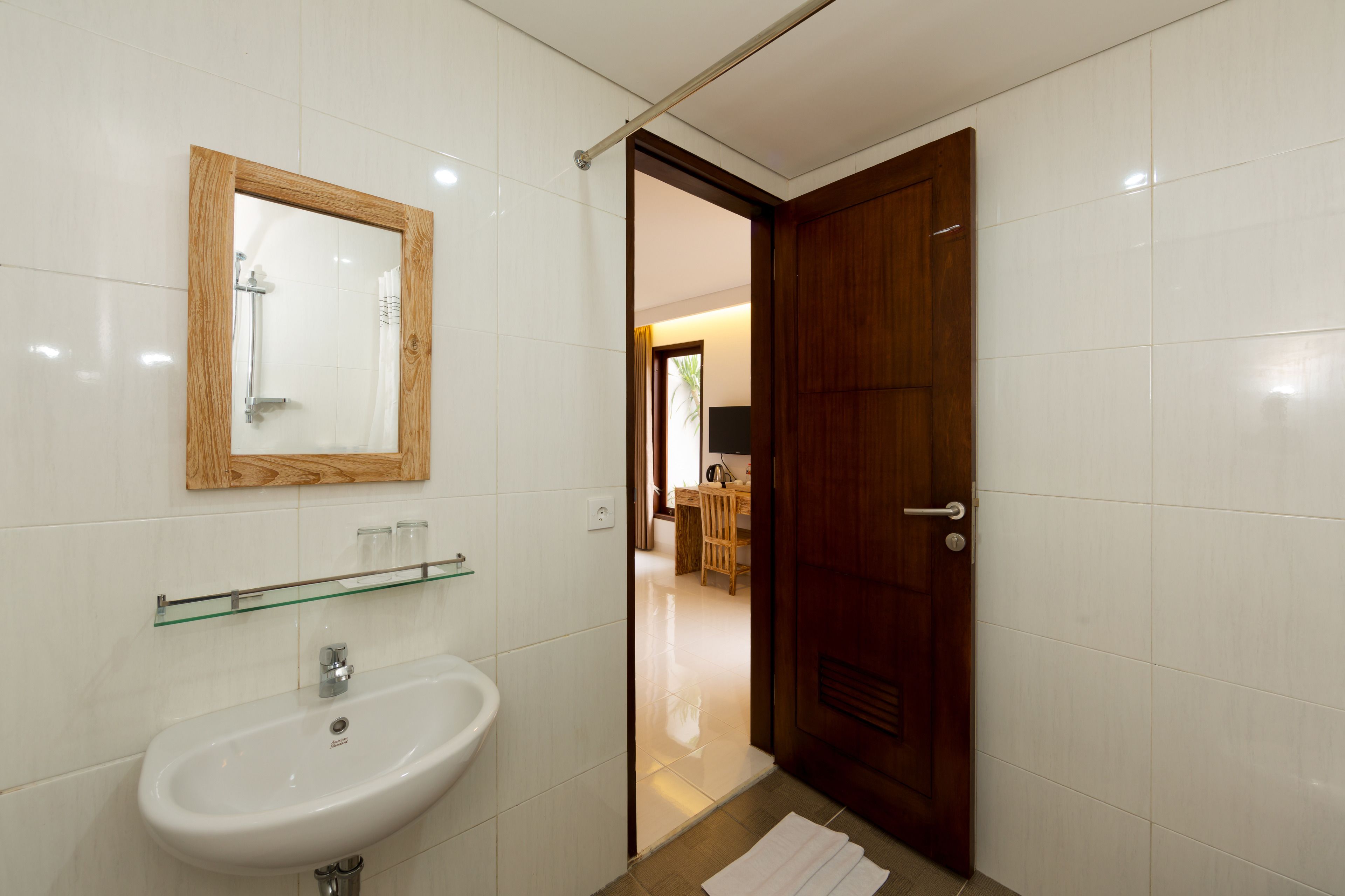 A bathroom with a white sink, a glass shelf, and a wooden-framed mirror.