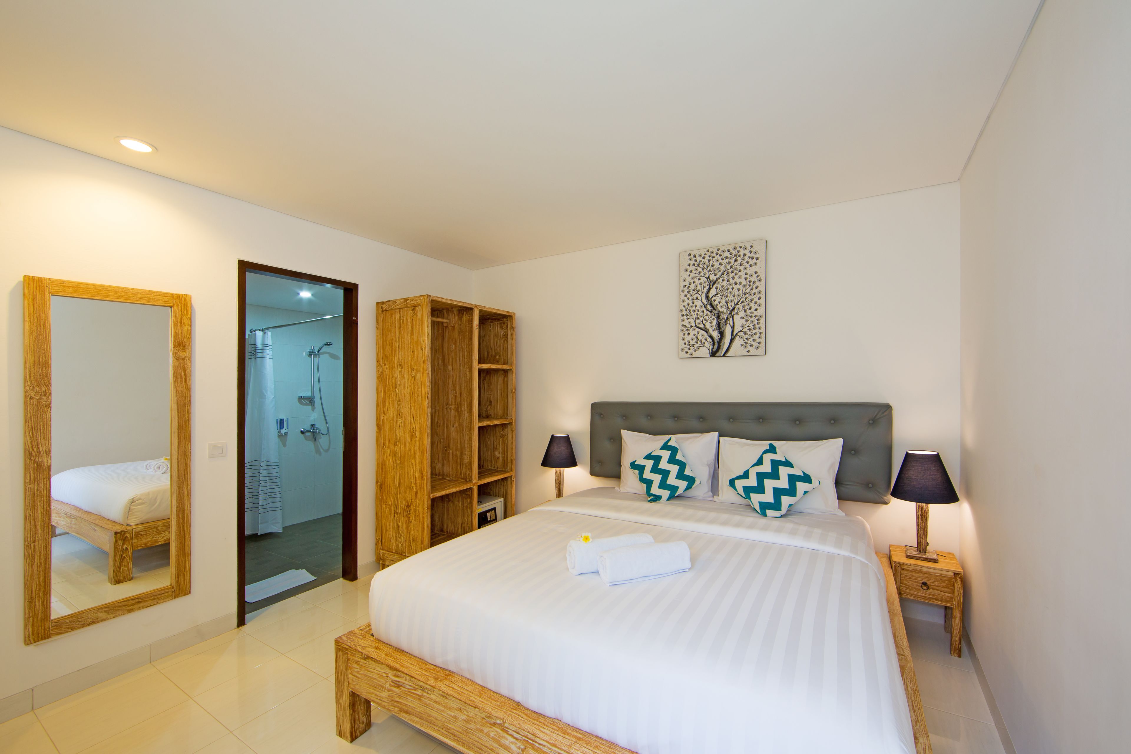 A bedroom with a large bed, wooden wardrobe, a mirror, and a wall-mounted artwork.