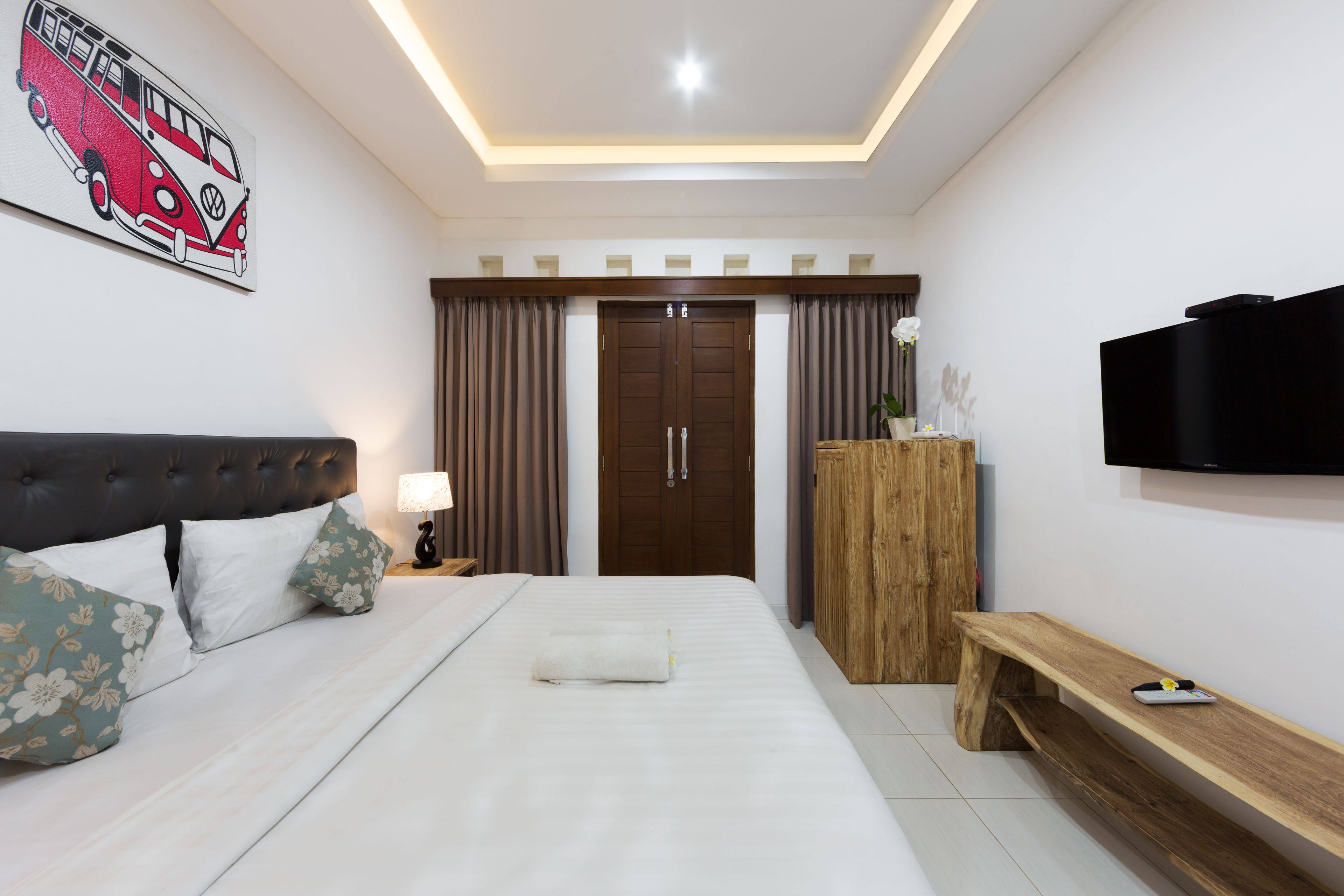 A bedroom with a bed, a TV, a wooden bench, a wardrobe, and a ceiling light.
