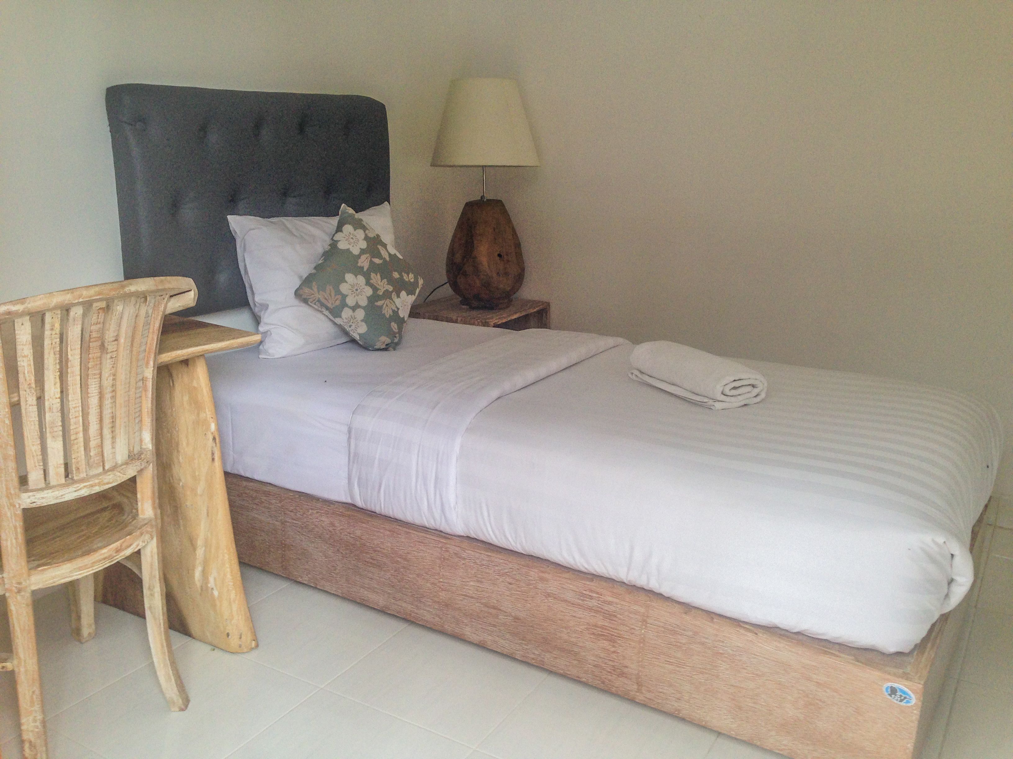 A bedroom with a wooden bed, a wooden chair, a bedside table with a lamp, and a pillow with a floral pattern.