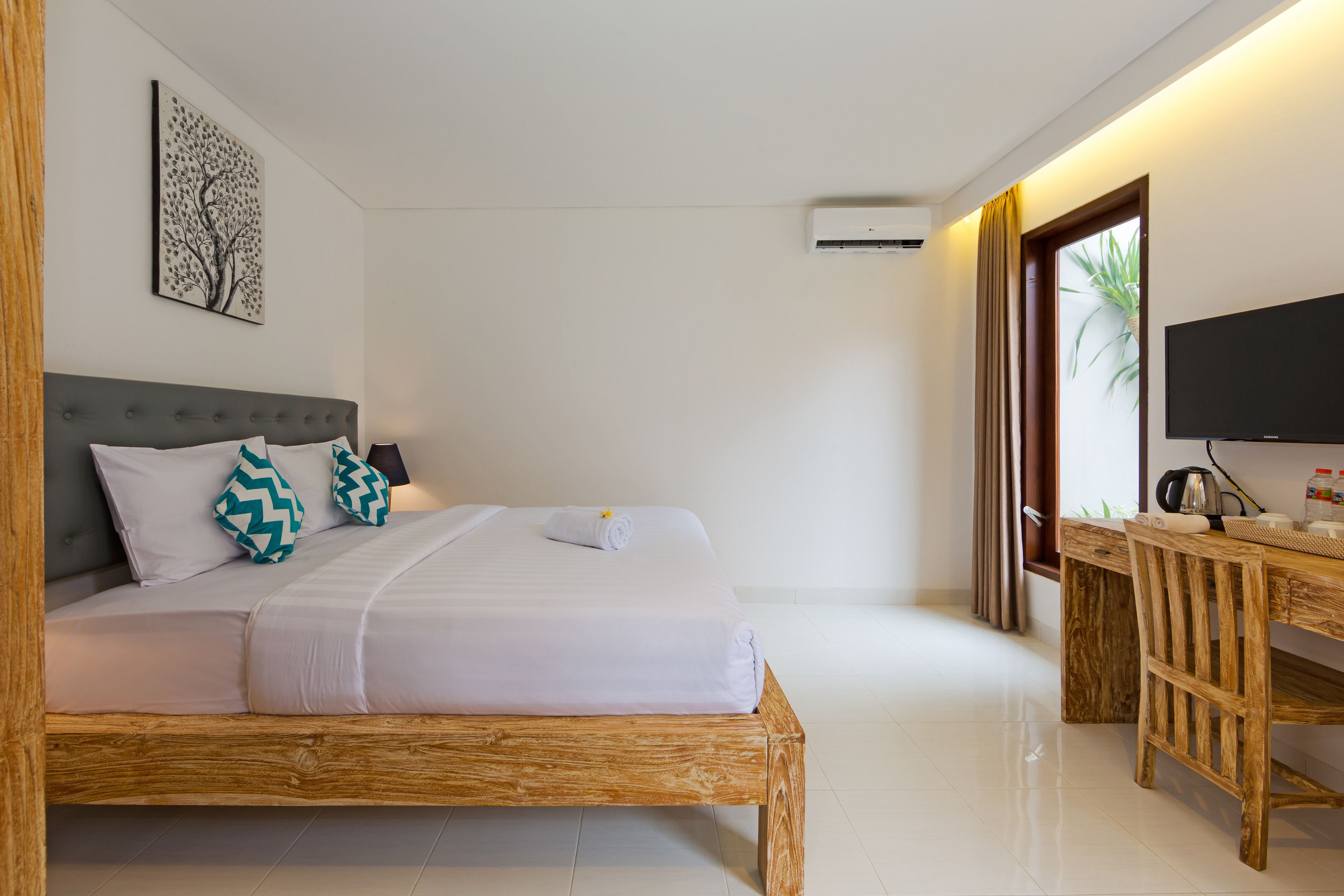 A bedroom with a wooden bed, a desk, a flat-screen TV, and a wall-mounted air conditioner.