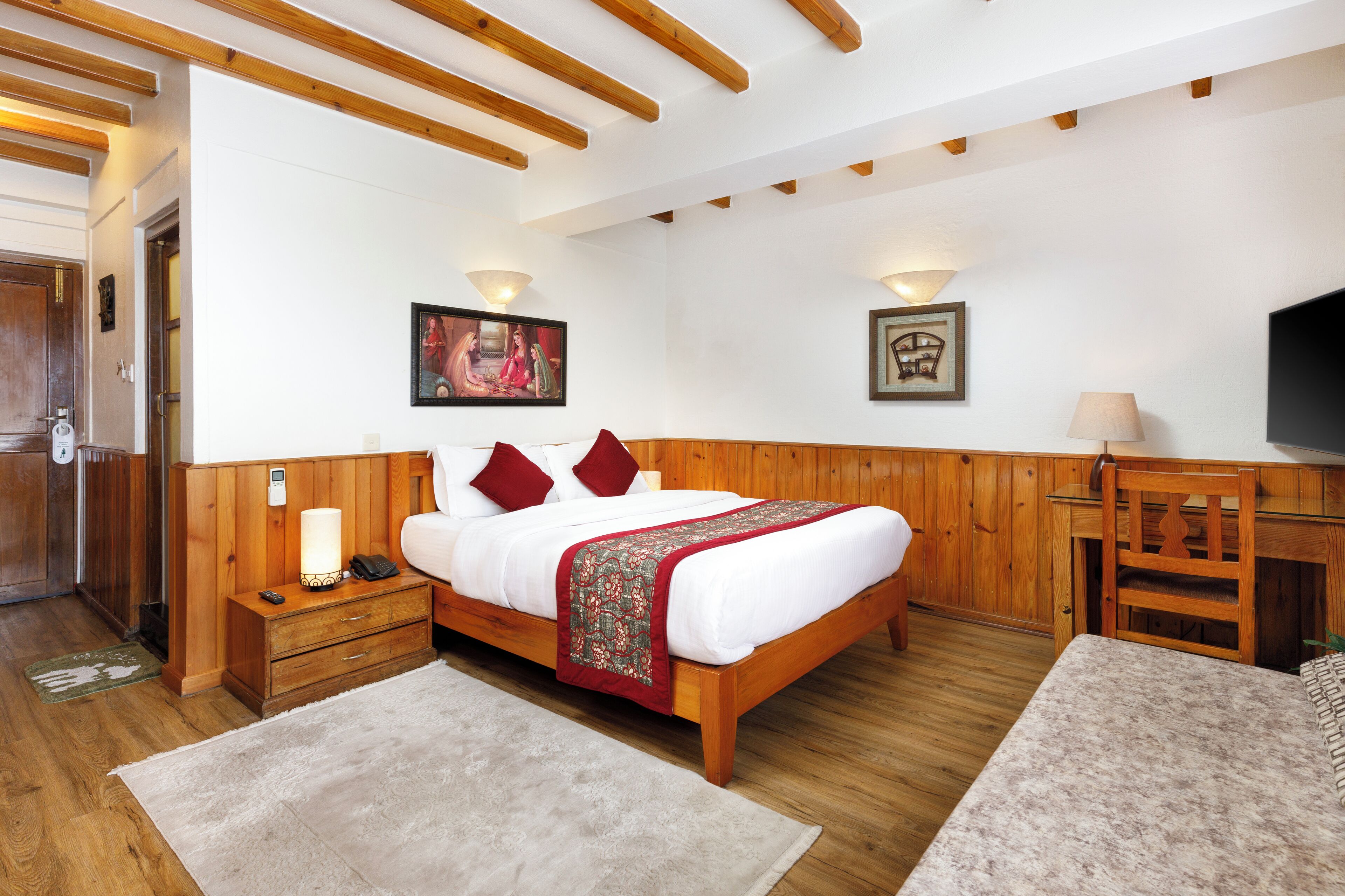 A bedroom with a wooden bed, bedside tables, a TV, and a desk.