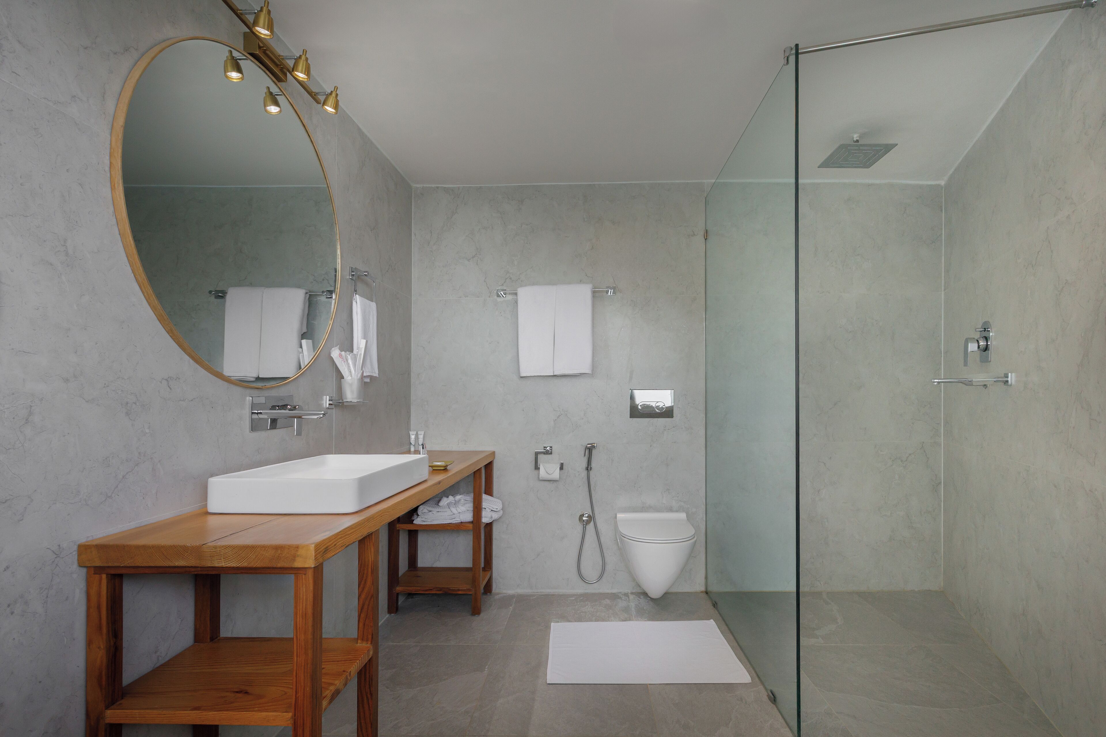 A modern bathroom with a wooden vanity, a large mirror, a glass-enclosed shower, and a white sink.