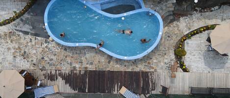 A swimming pool with a stone border, surrounded by a wooden deck and a stone wall.